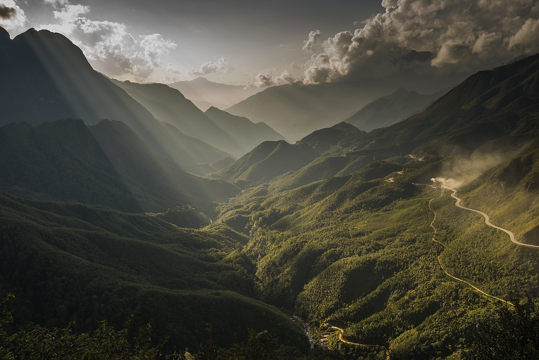 Sun rays over a mountain valley with a winding road HD Wallpaper