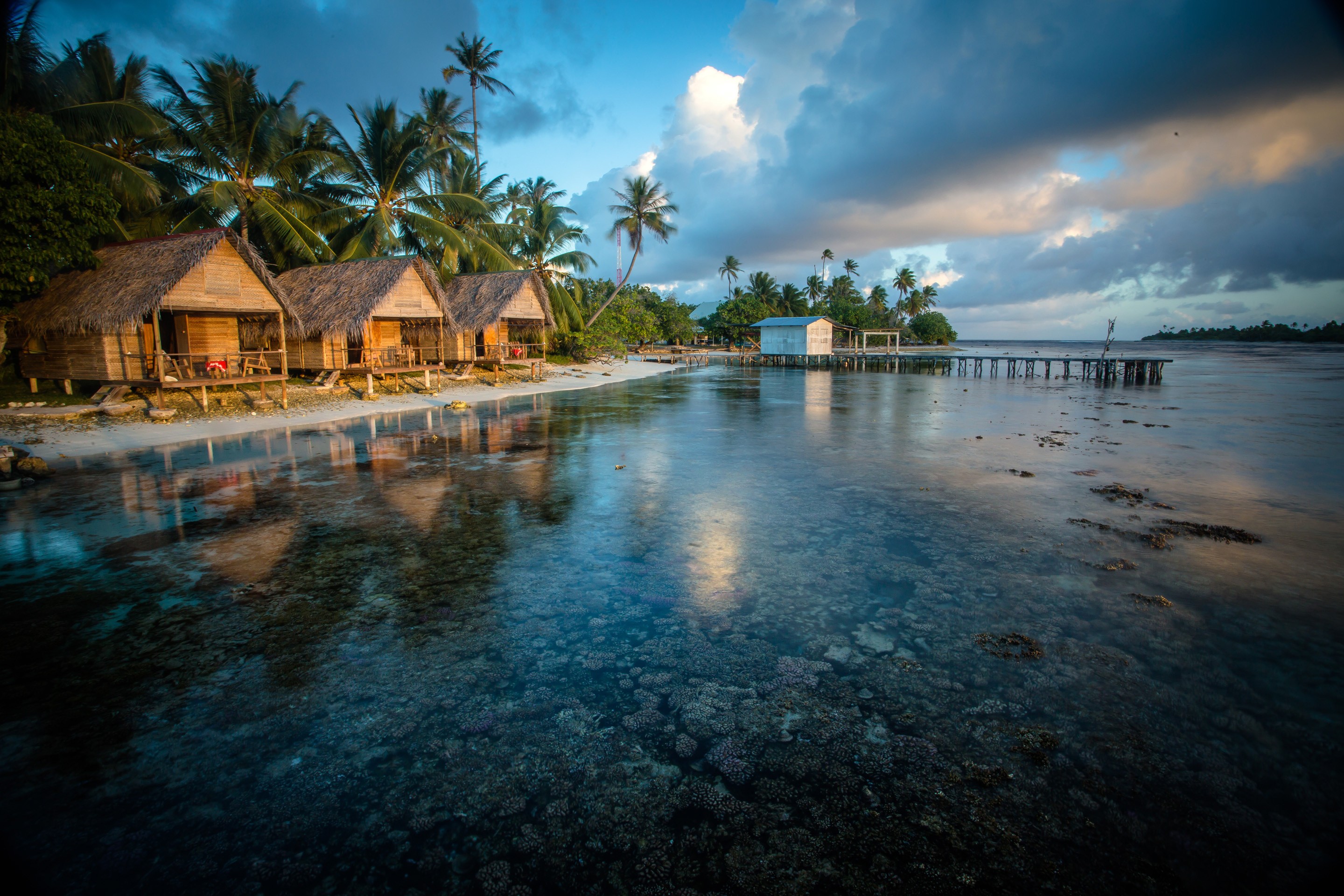 Tropical bungalows on a beach with clear water and coral reefs HD Wallpaper