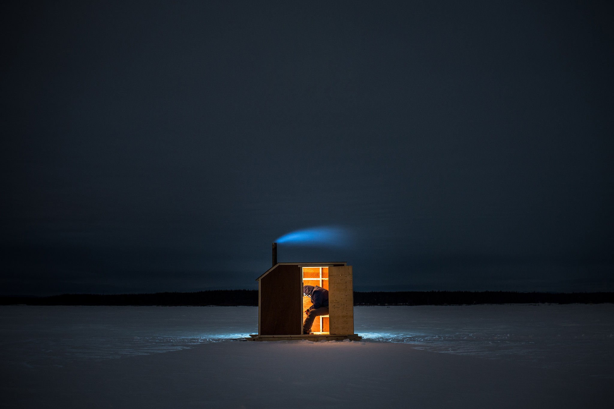 Person ice fishing in a small hut at night HD Wallpaper