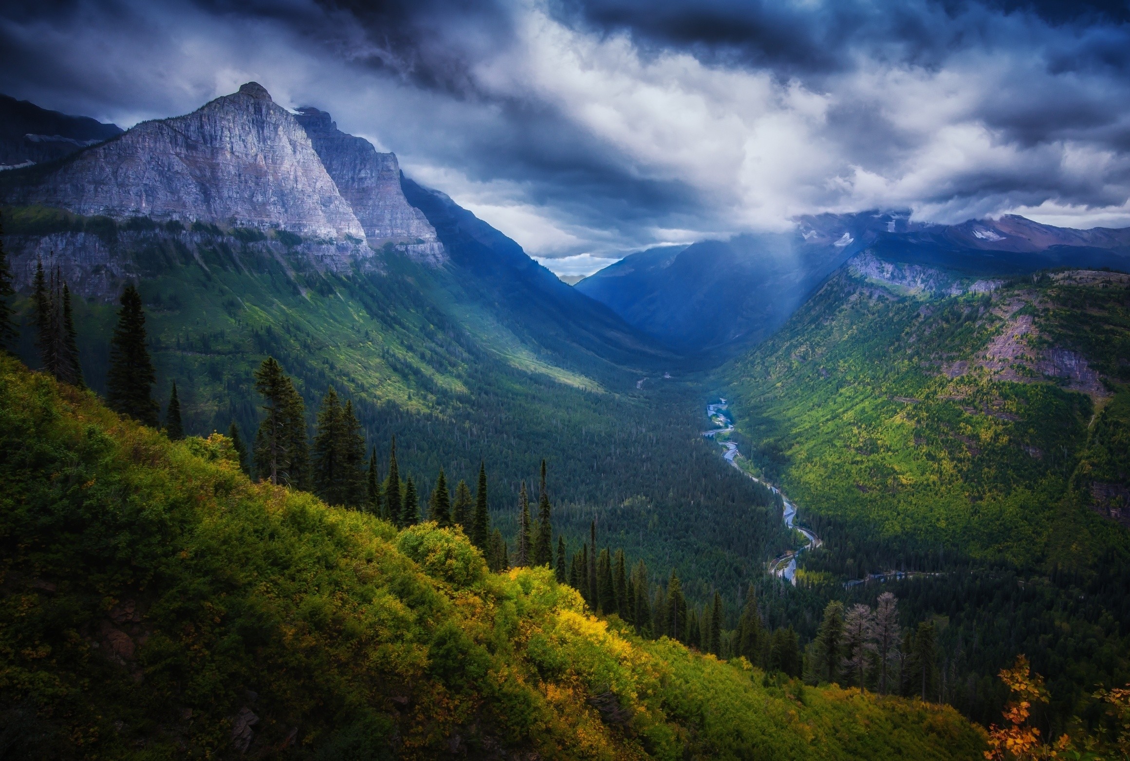 Valley with mountains, river, and forest under dramatic clouds HD Wallpaper