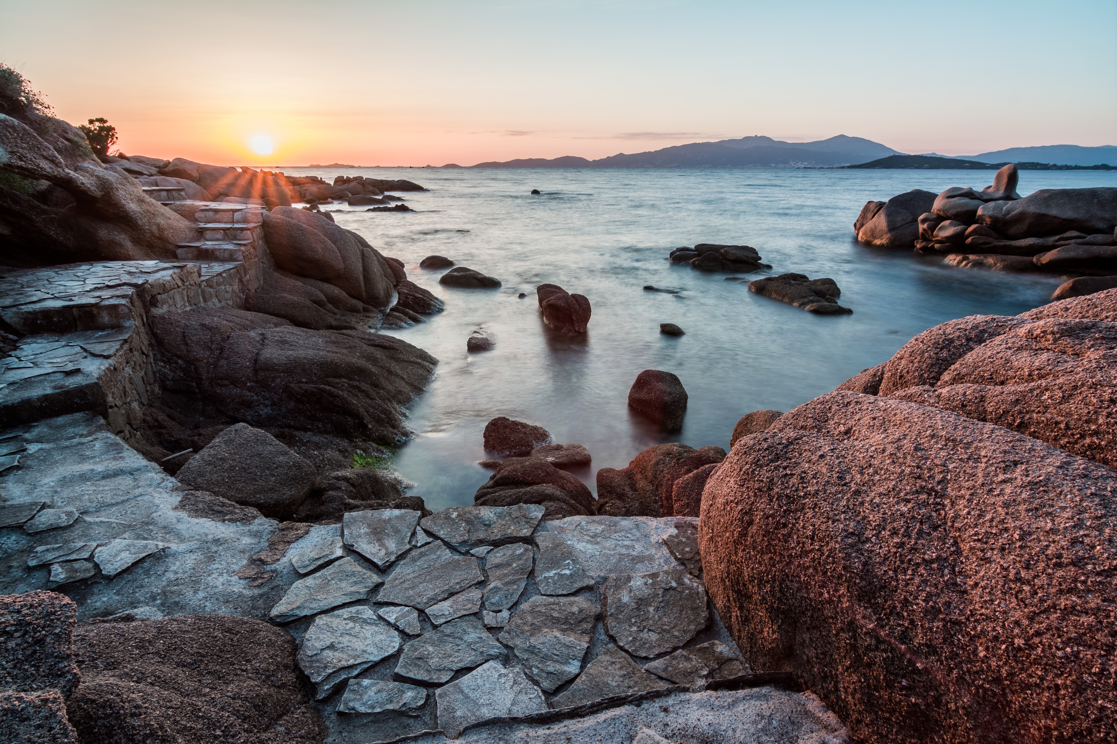 Rocky coastline with stairs at sunset in Corsica HD Wallpaper