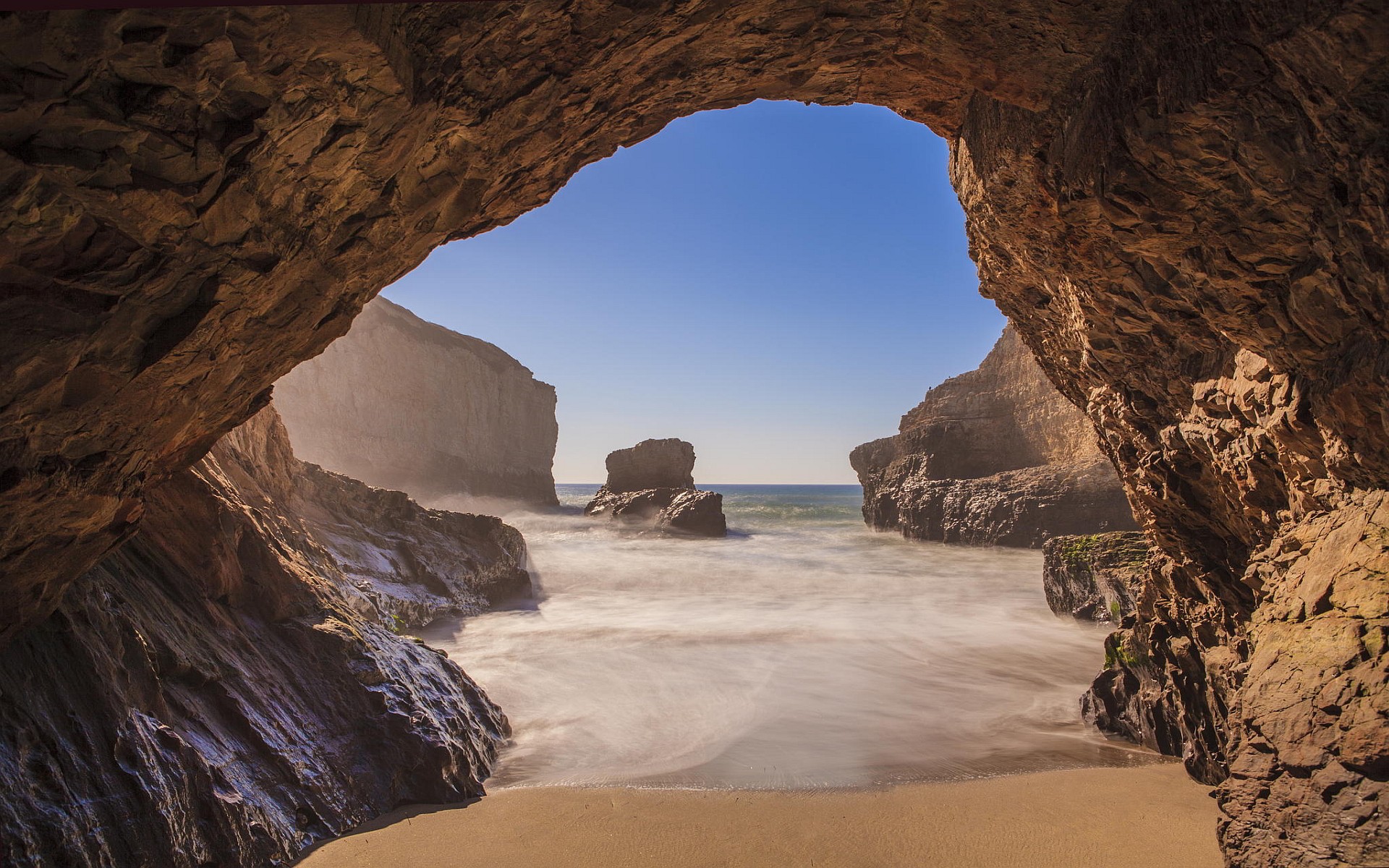 Cave entrance overlooking a sandy beach and the sea HD Wallpaper