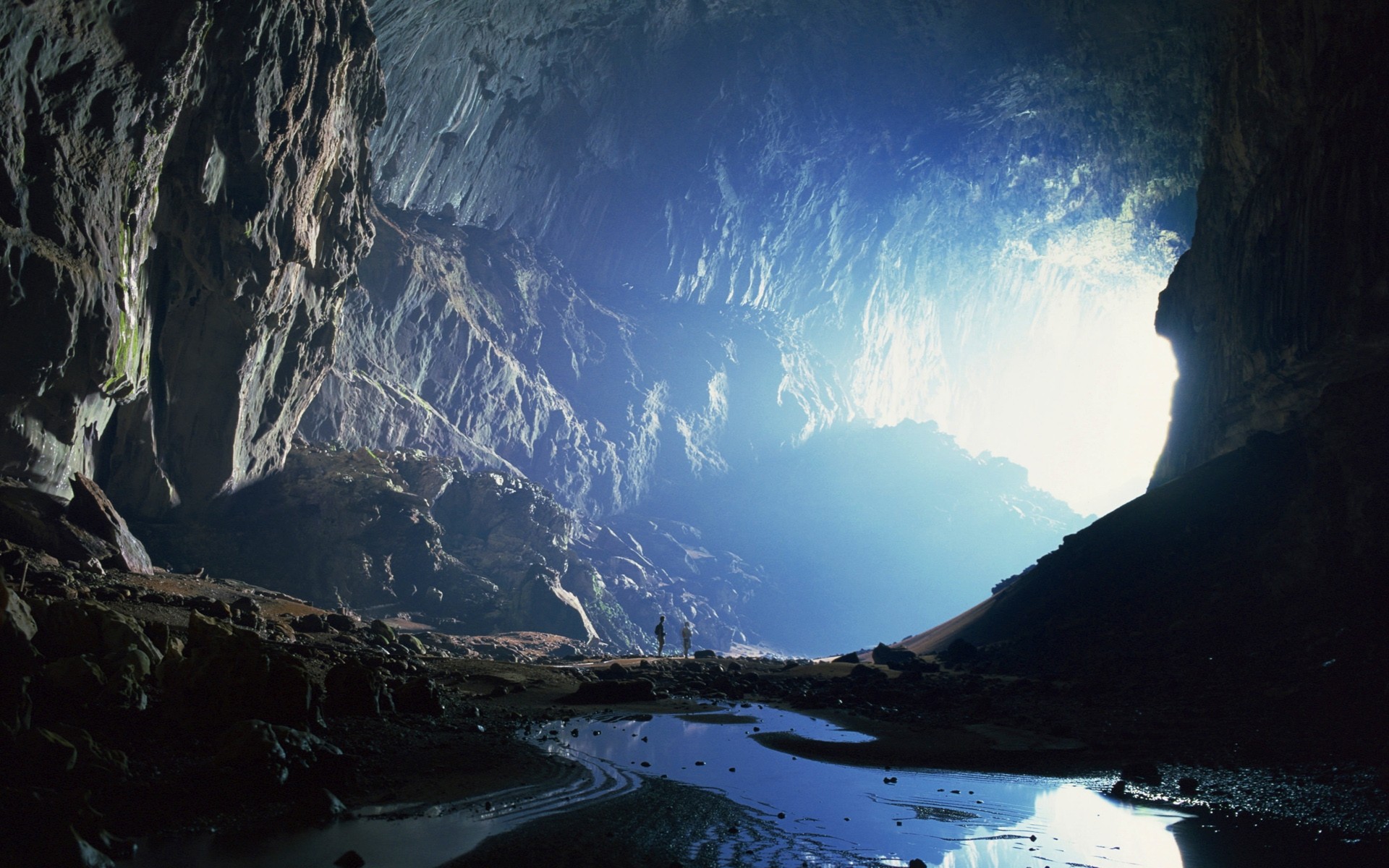 Two people stand in a vast cave in Malaysia HD Wallpaper