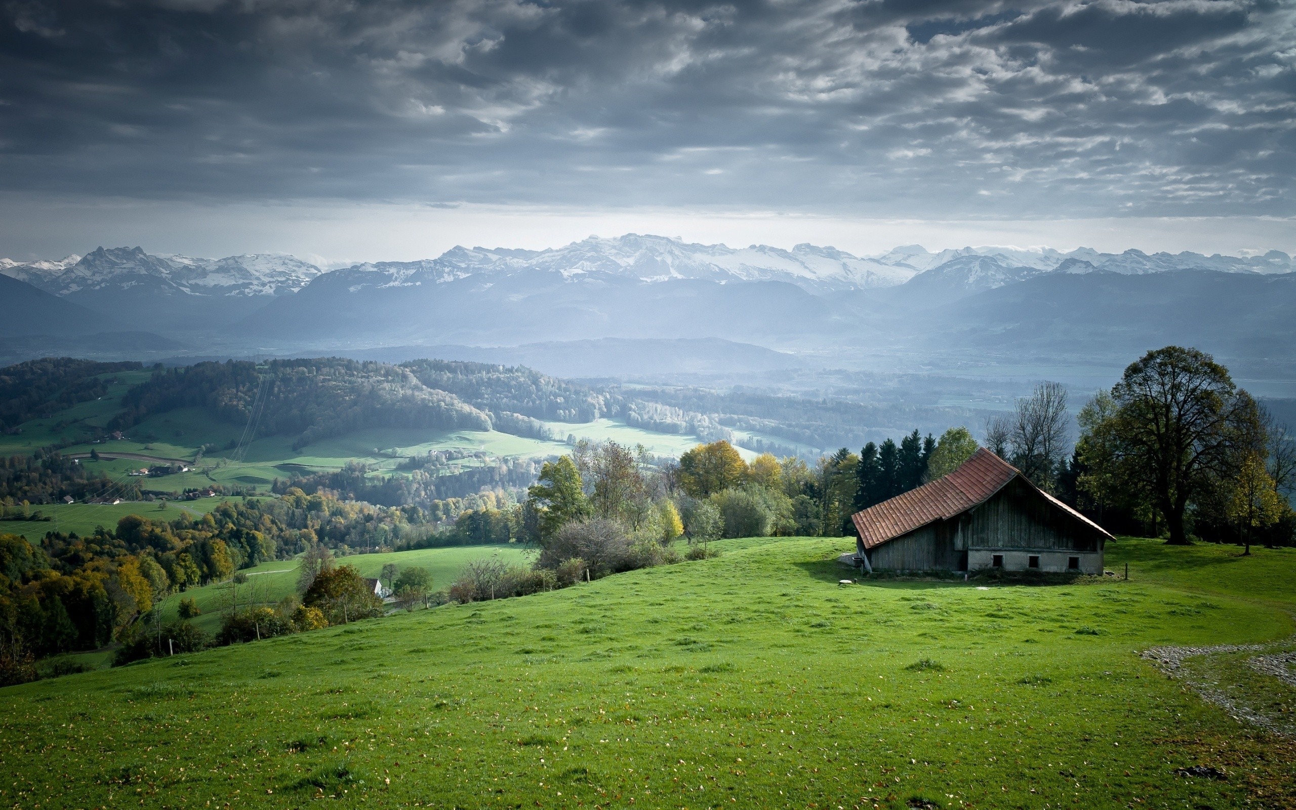 Barn on a grassy hill with mountains in the background HD Wallpaper
