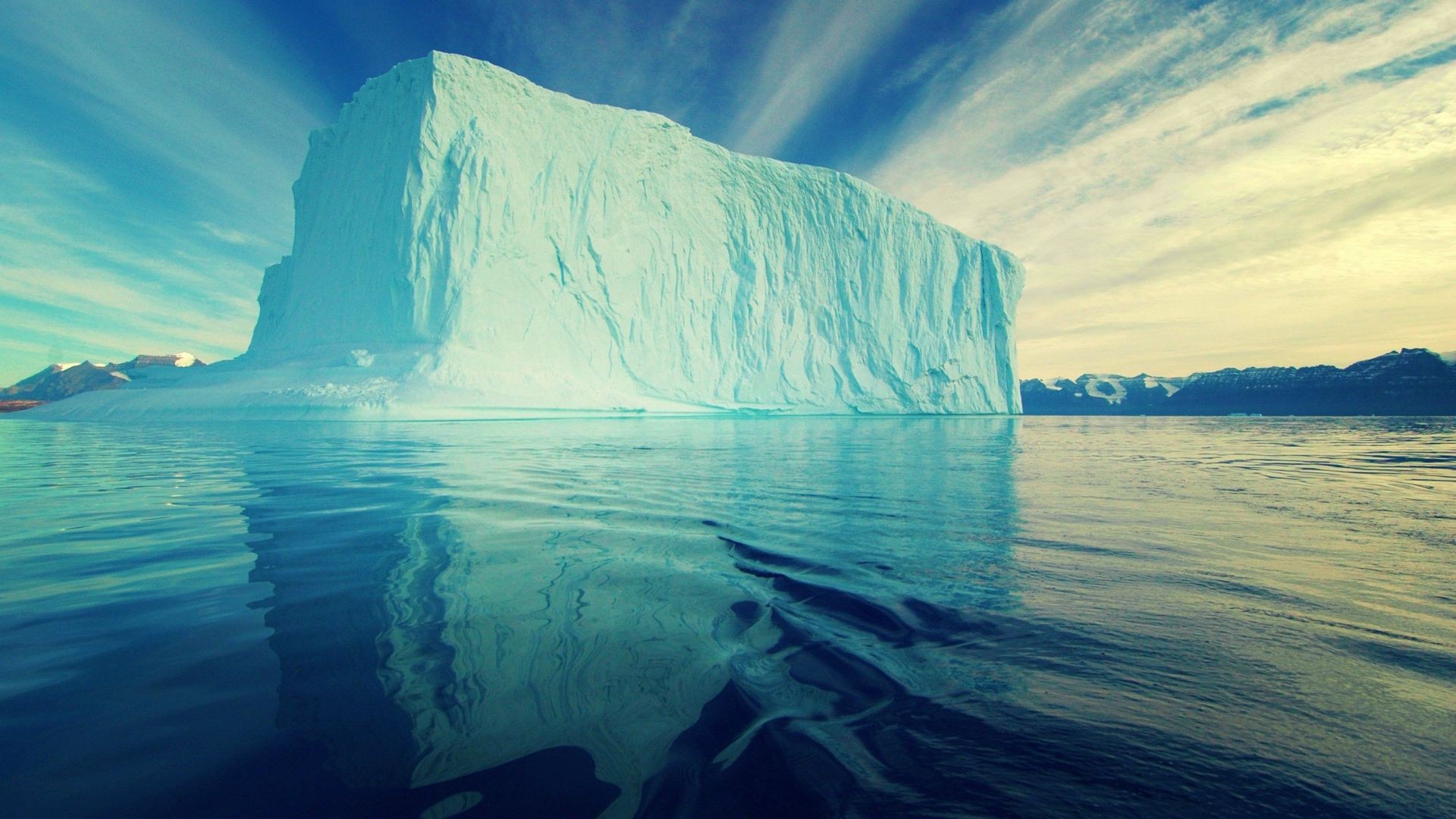 Massive iceberg floating in the ocean with mountains in the background HD Wallpaper