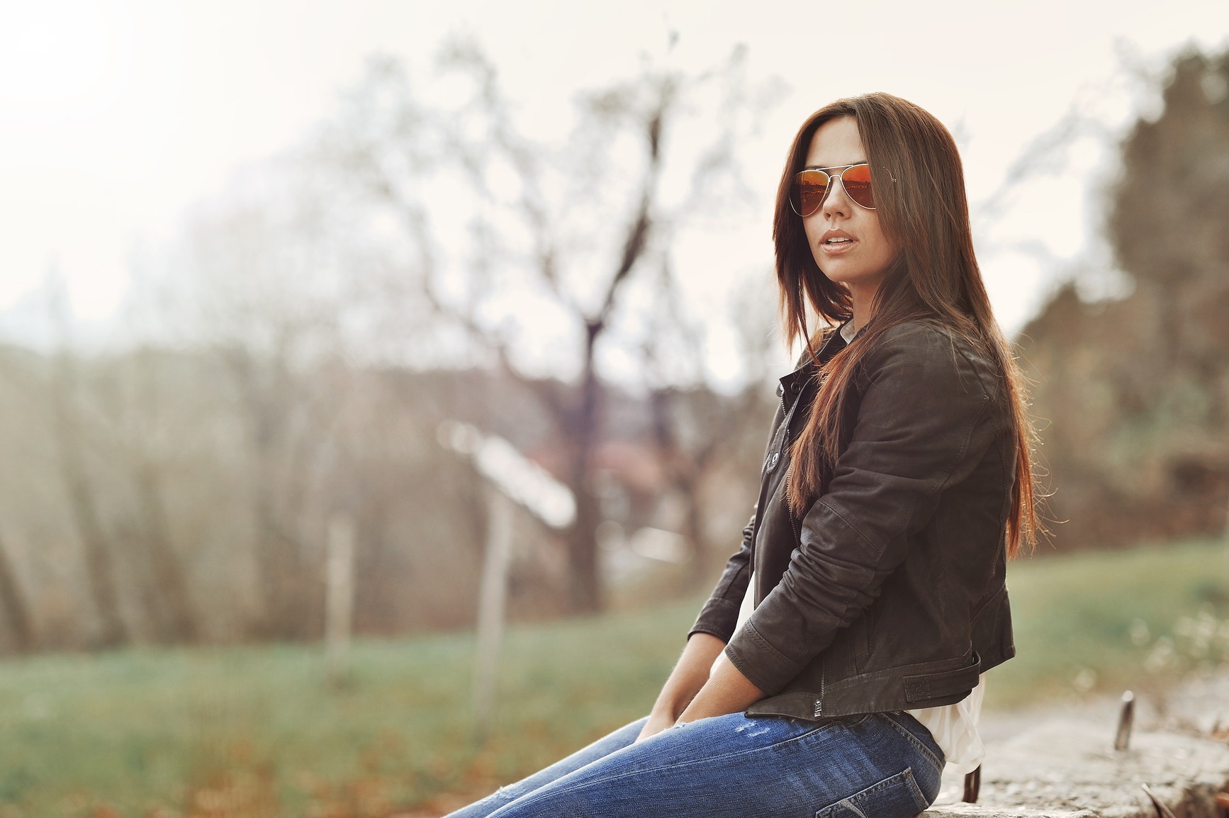Woman with sunglasses and jeans sitting outdoors HD Wallpaper