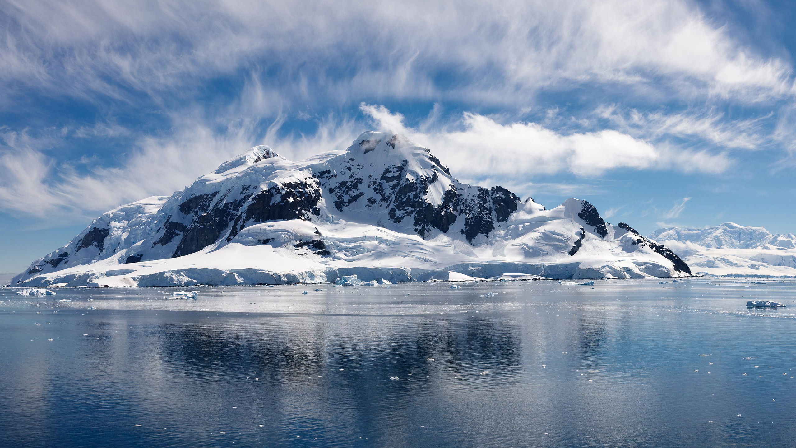Snow-covered mountains reflected in the water under a cloudy sky HD Wallpaper