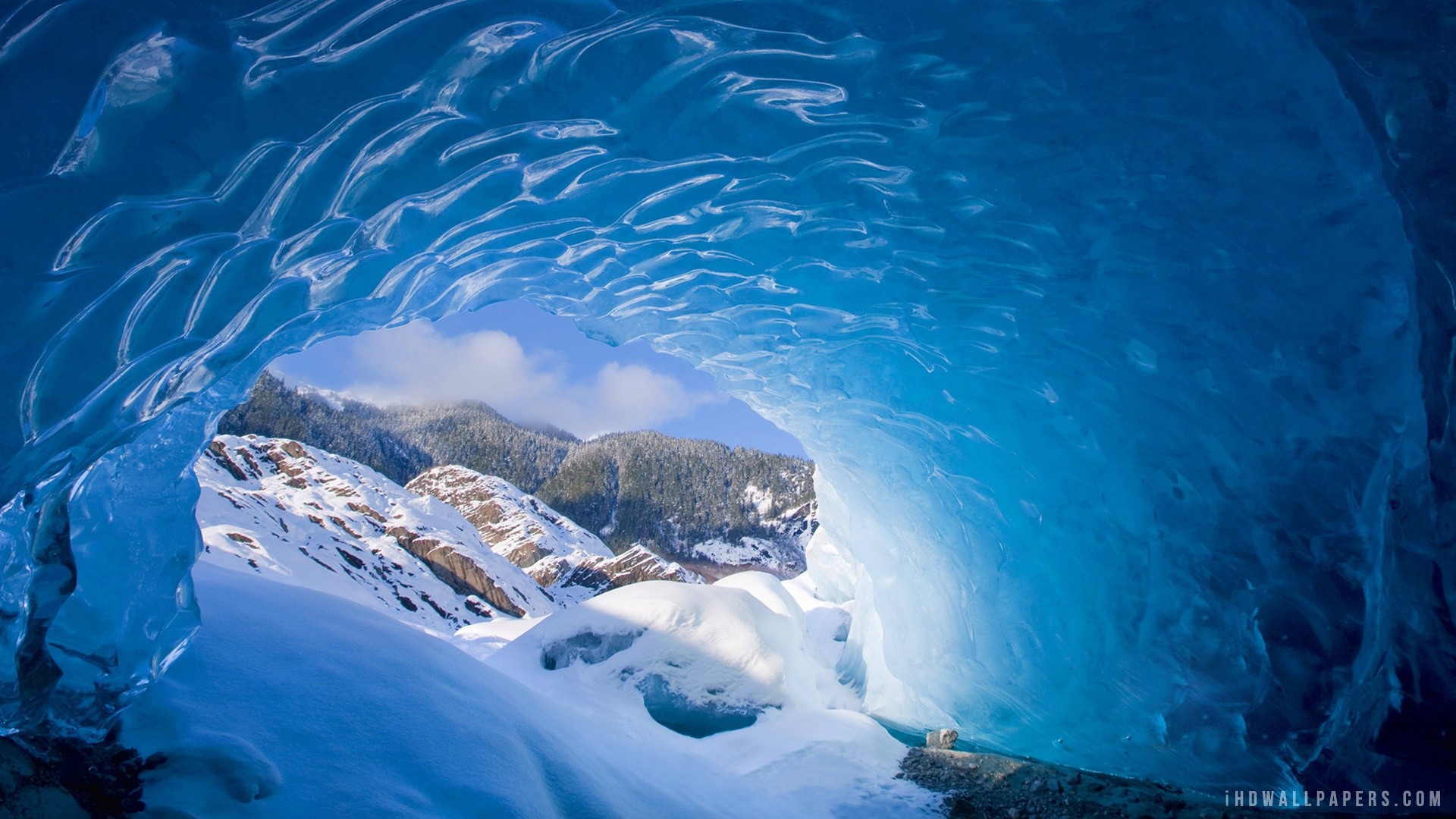 Inside a blue ice cave looking out at snowy mountains HD Wallpaper