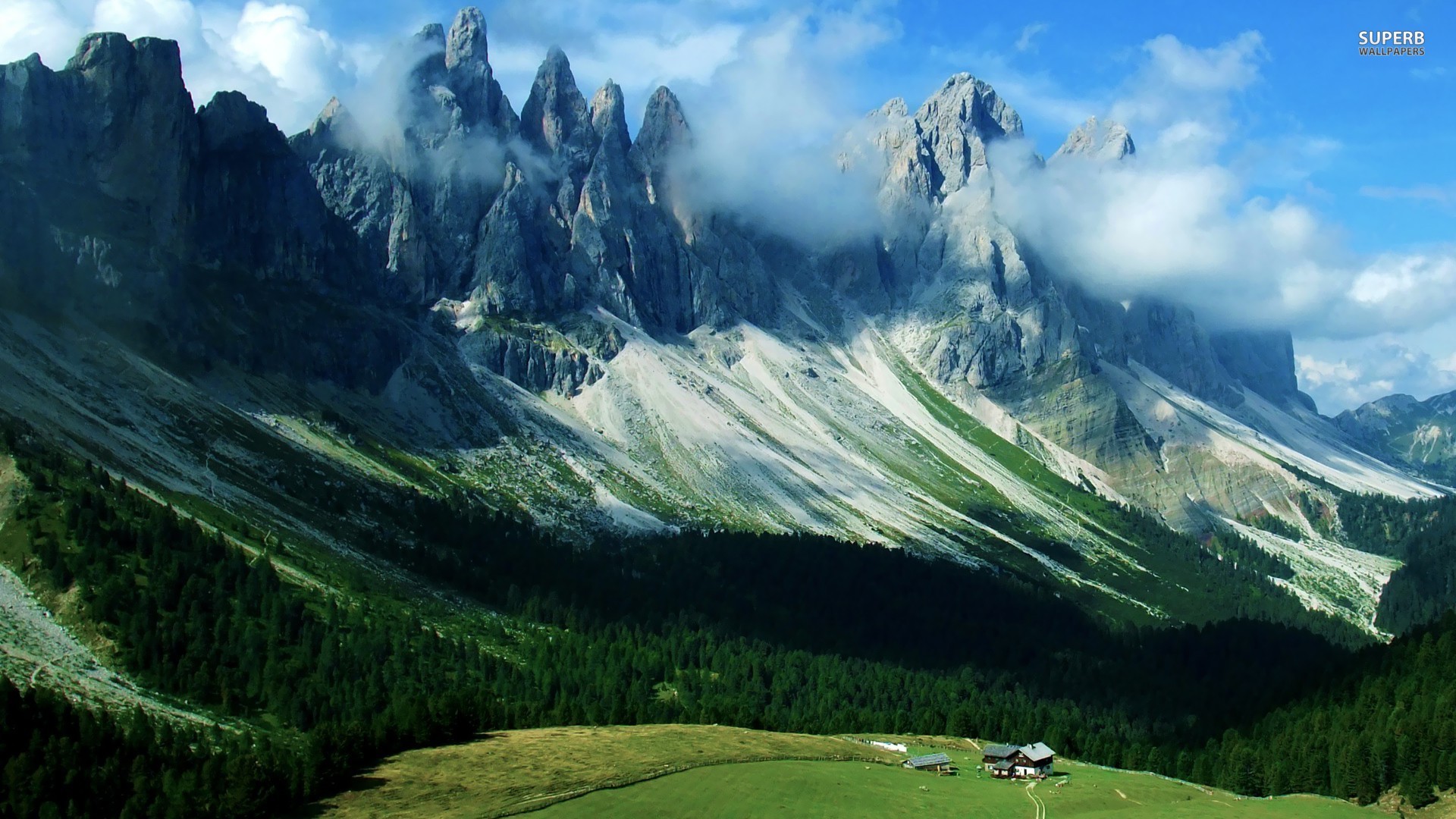 Mountain peaks with clouds and a forest below HD Wallpaper