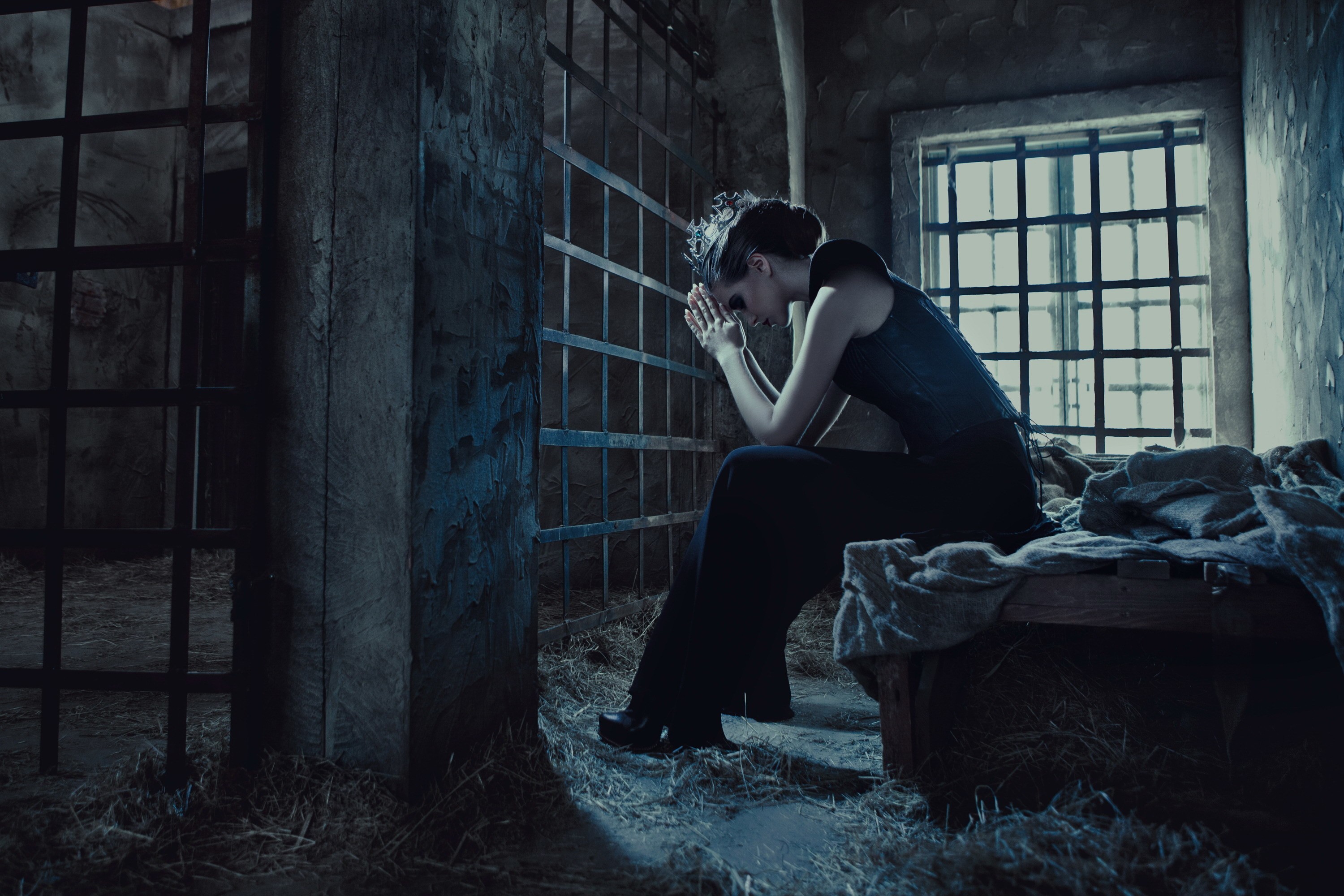 Woman praying in a prison cell with barred window HD Wallpaper