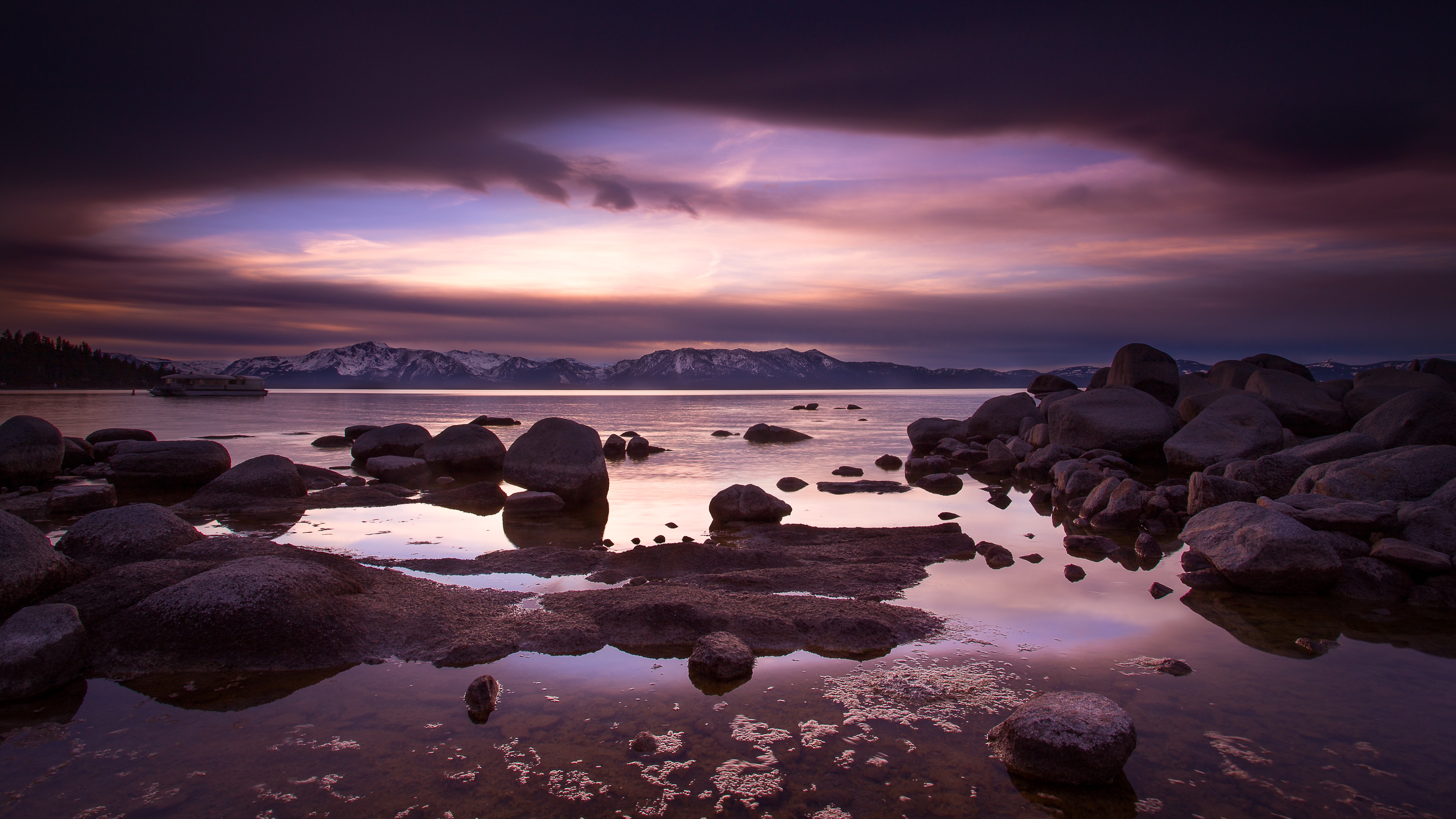 Rocky lake shore at sunset with mountains in the distance HD Wallpaper