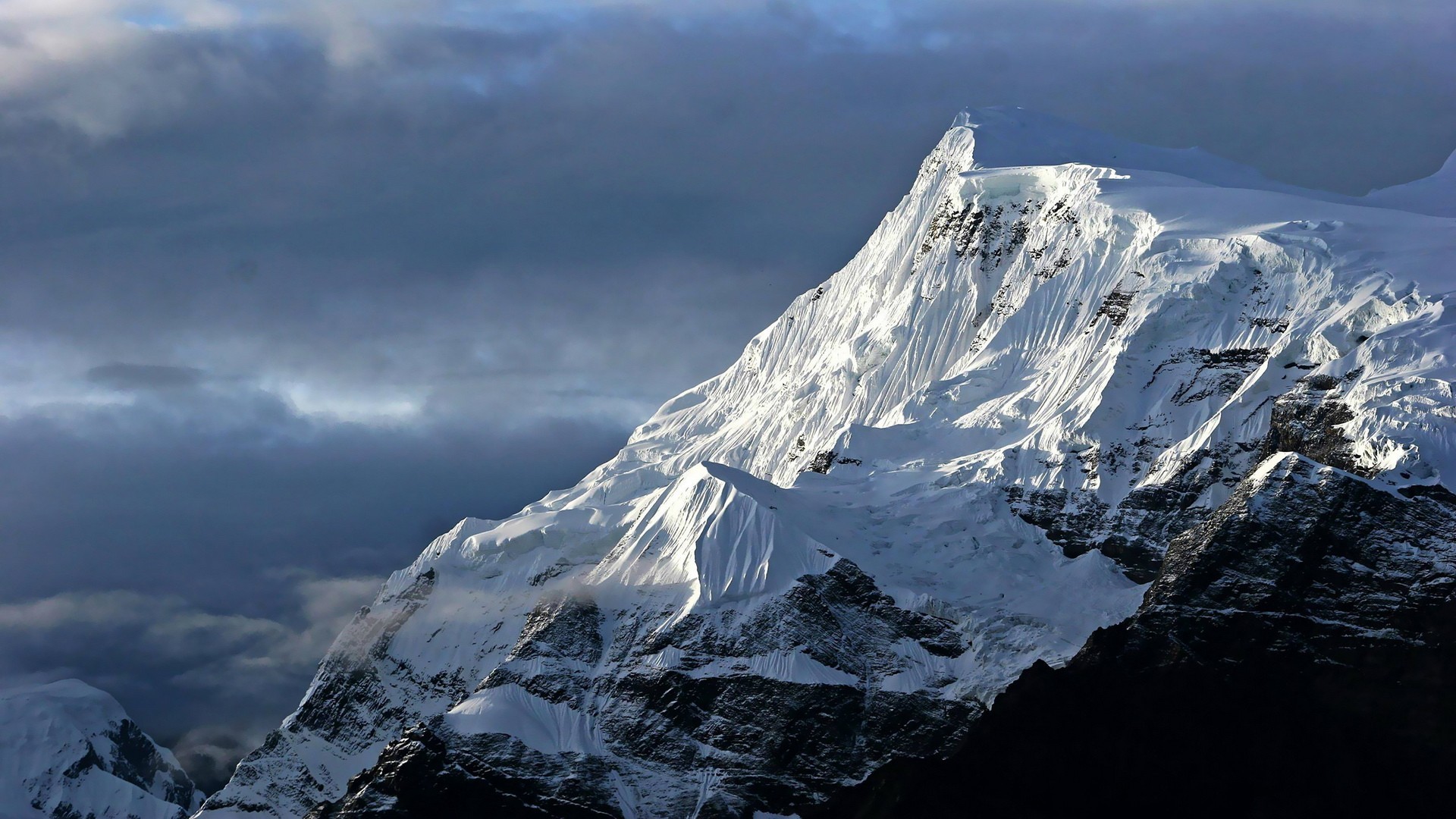 Snow-covered mountain peak under dramatic clouds HD Wallpaper