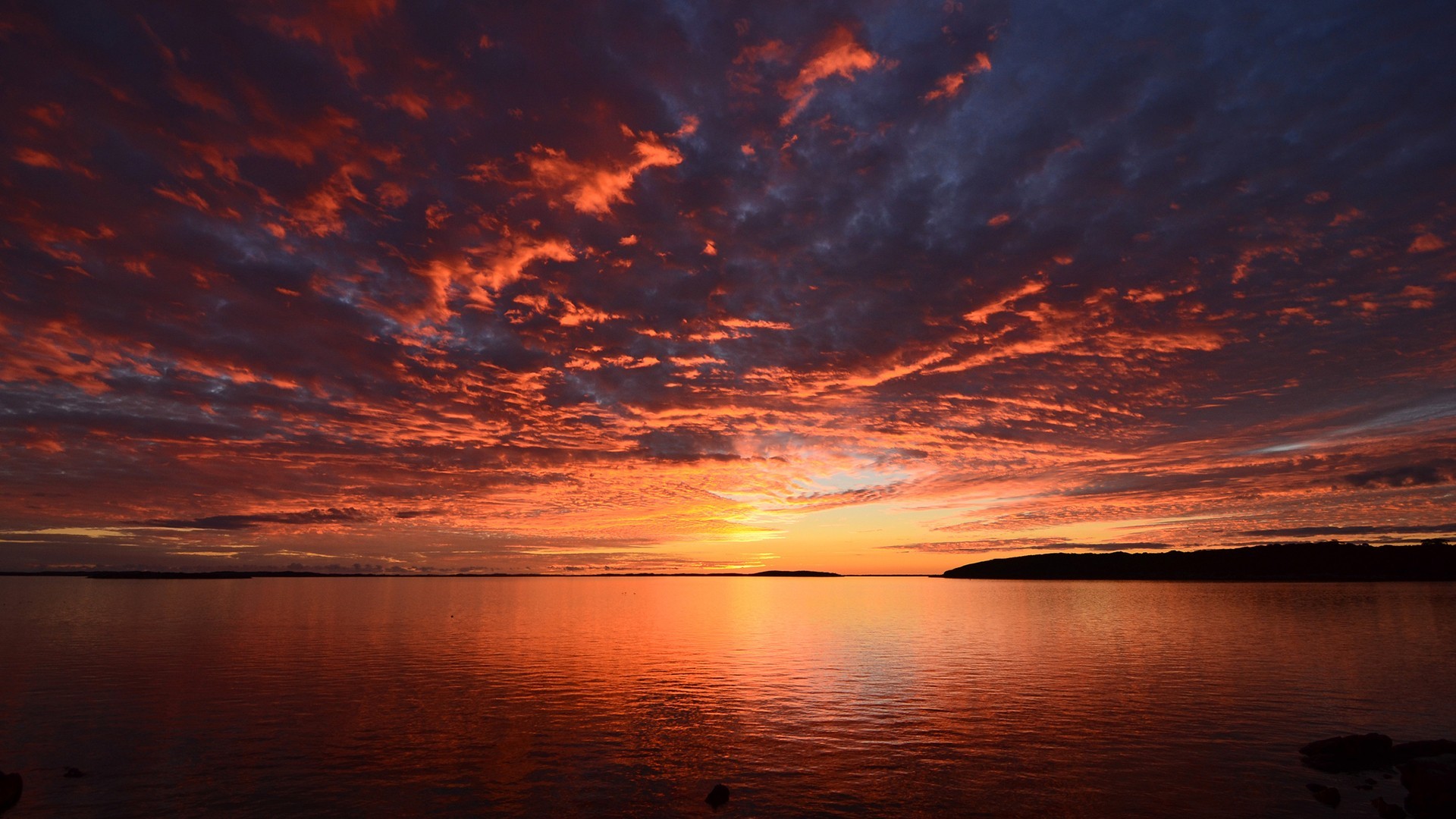 Sunset over a calm body of water with dramatic clouds HD Wallpaper