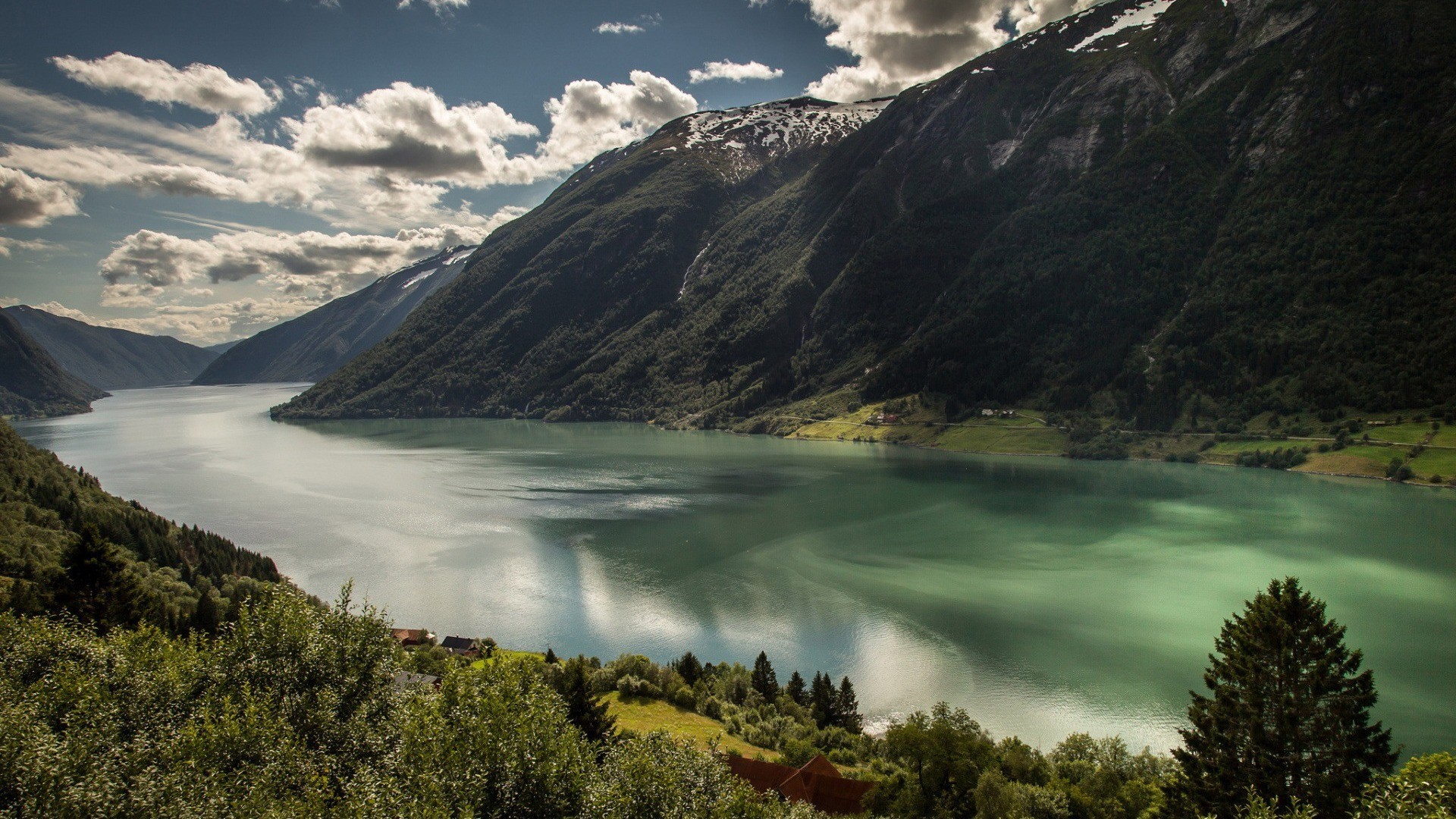 A vast fjord surrounded by green mountains under a cloudy sky HD Wallpaper