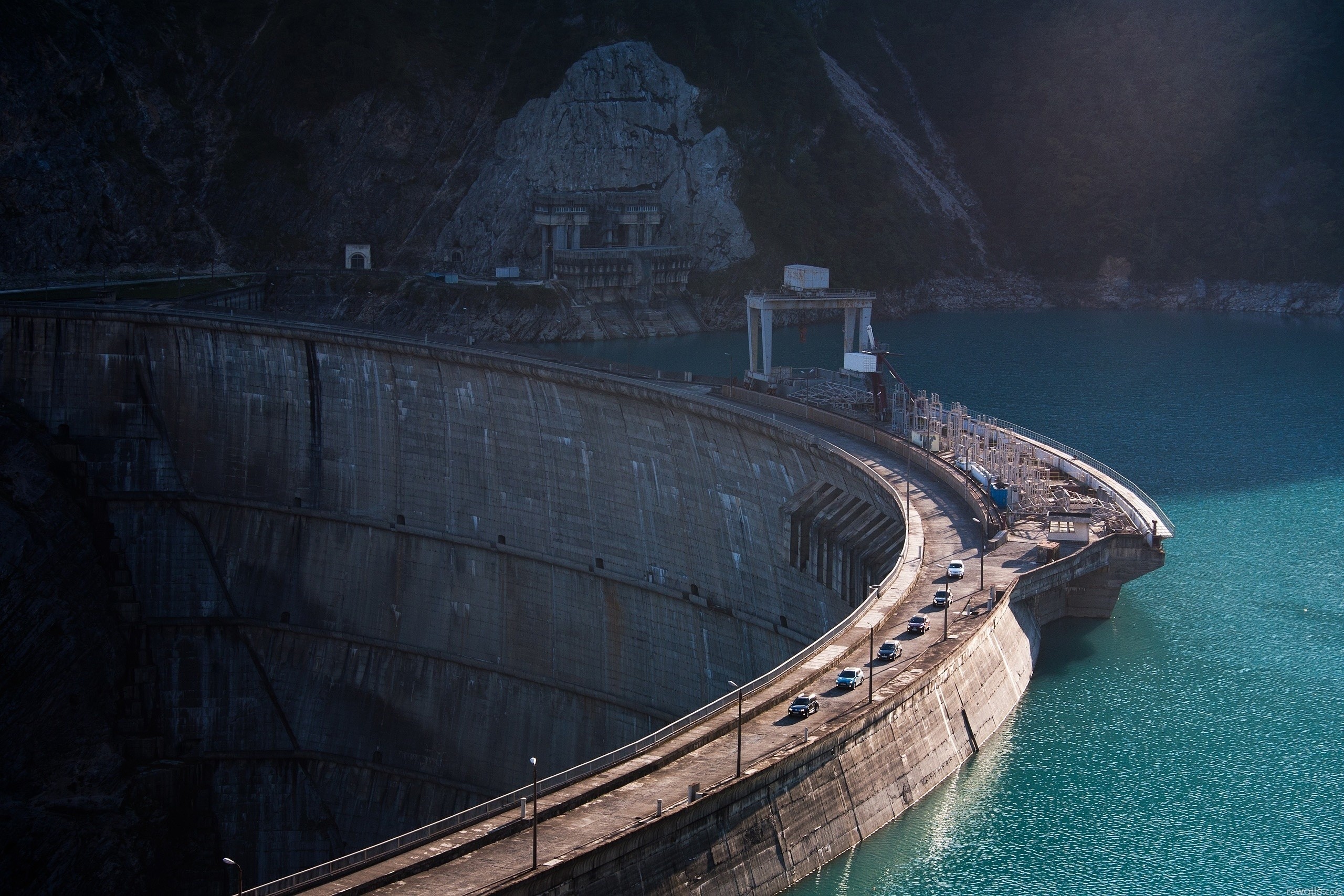 Curved concrete dam with cars on top and mountains HD Wallpaper
