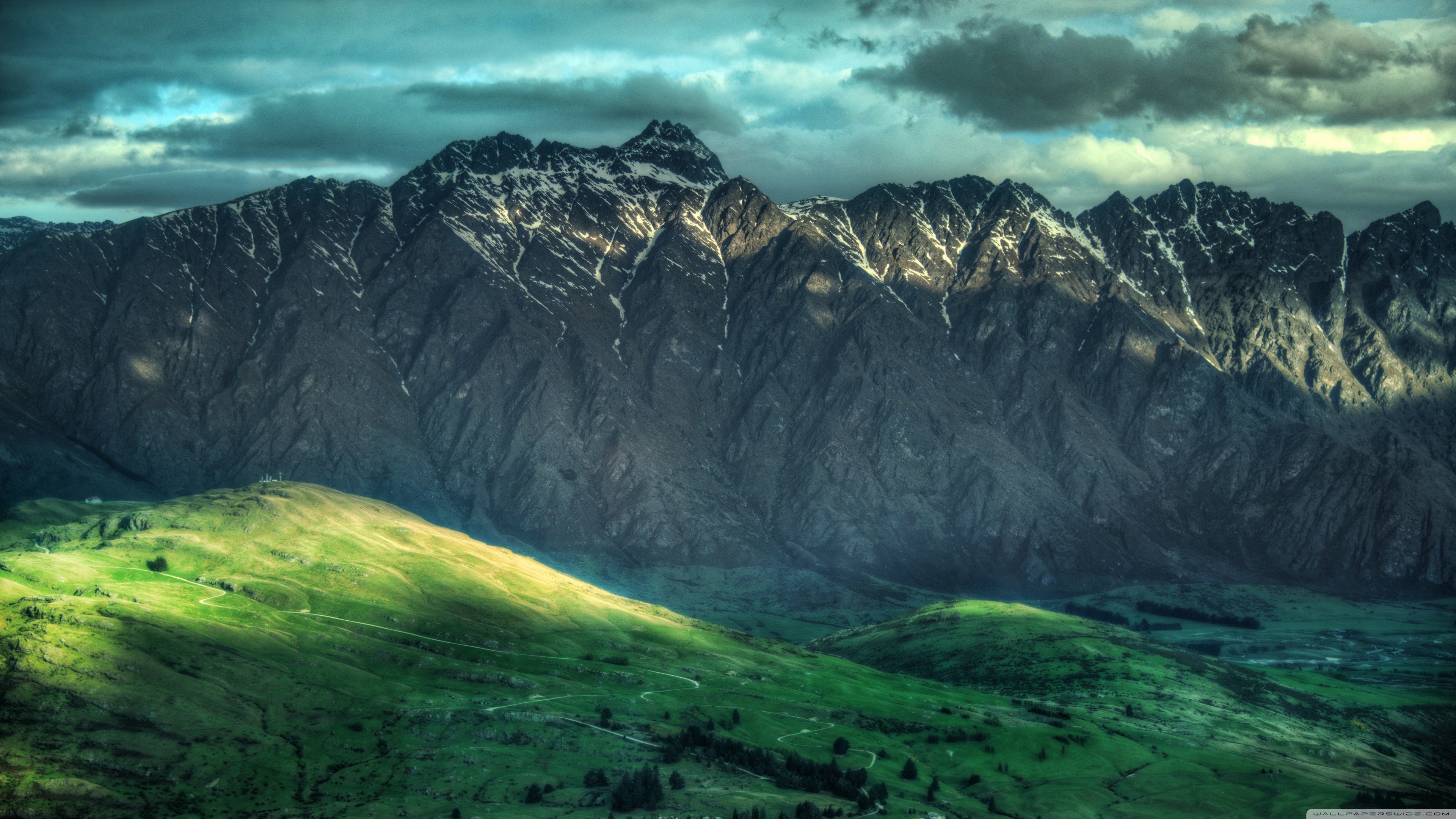Mountains and green fields under a cloudy sky HD Wallpaper