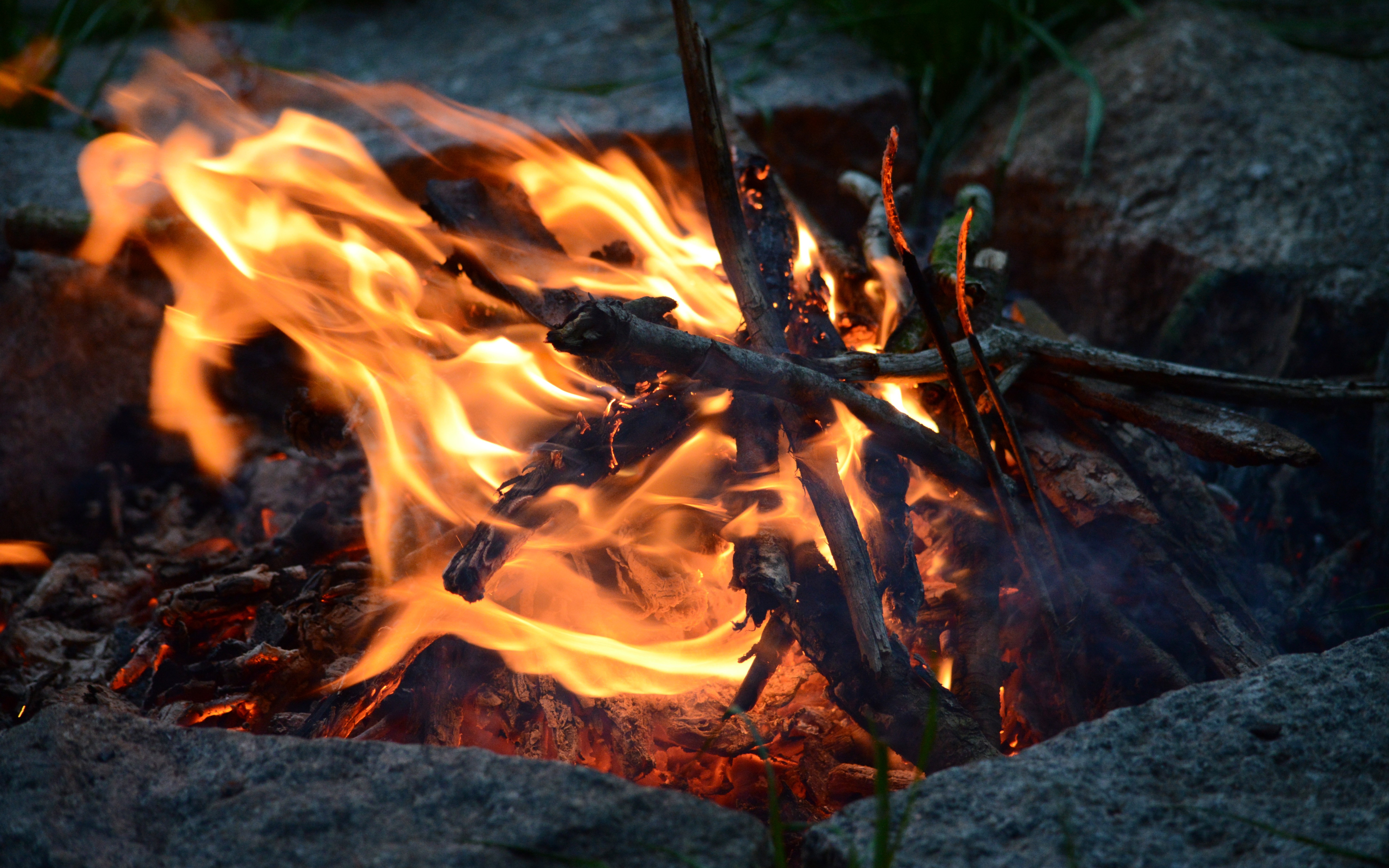 Campfire burning among rocks and grass HD Wallpaper