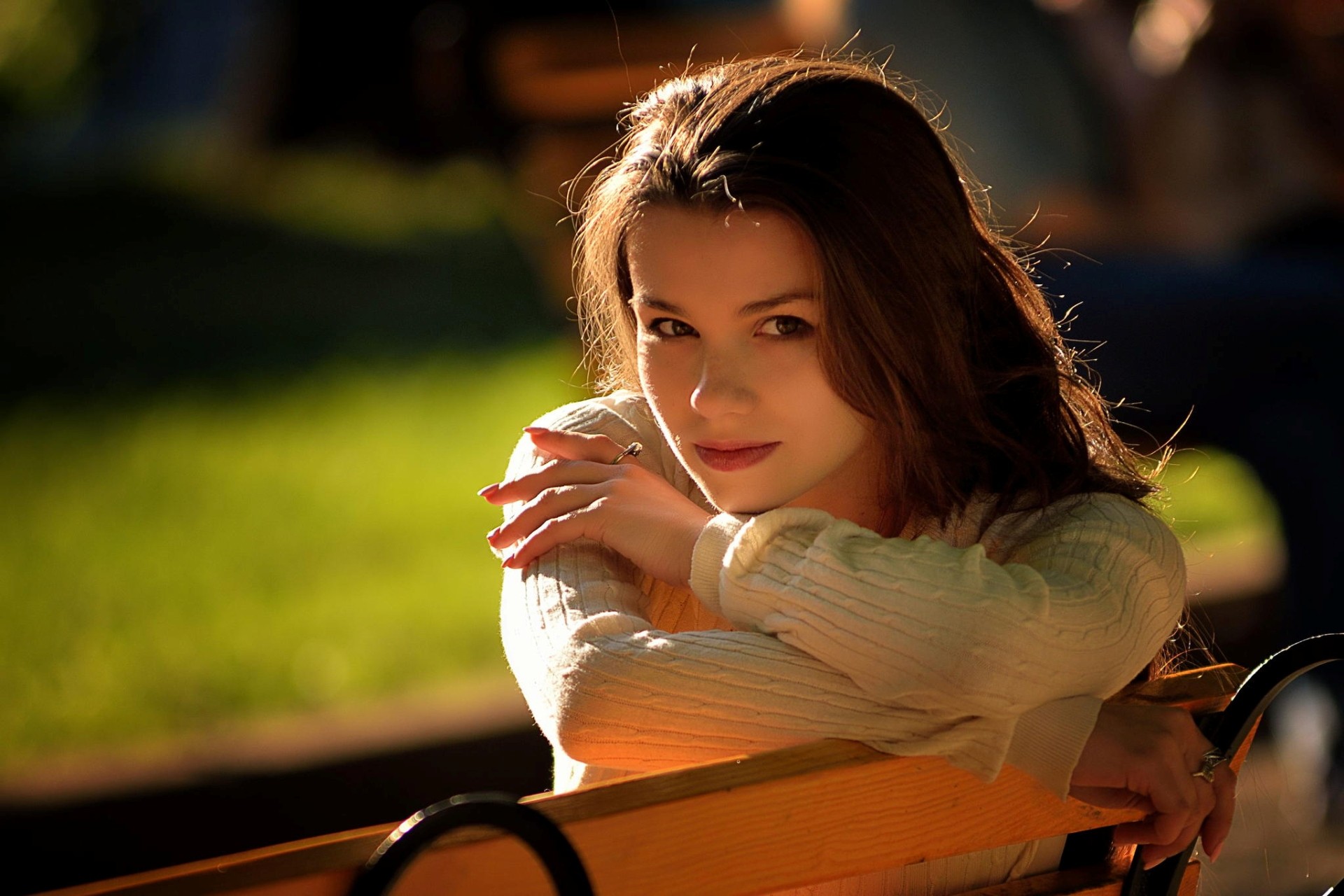 Woman with brown eyes wearing a sweater on a bench HD Wallpaper
