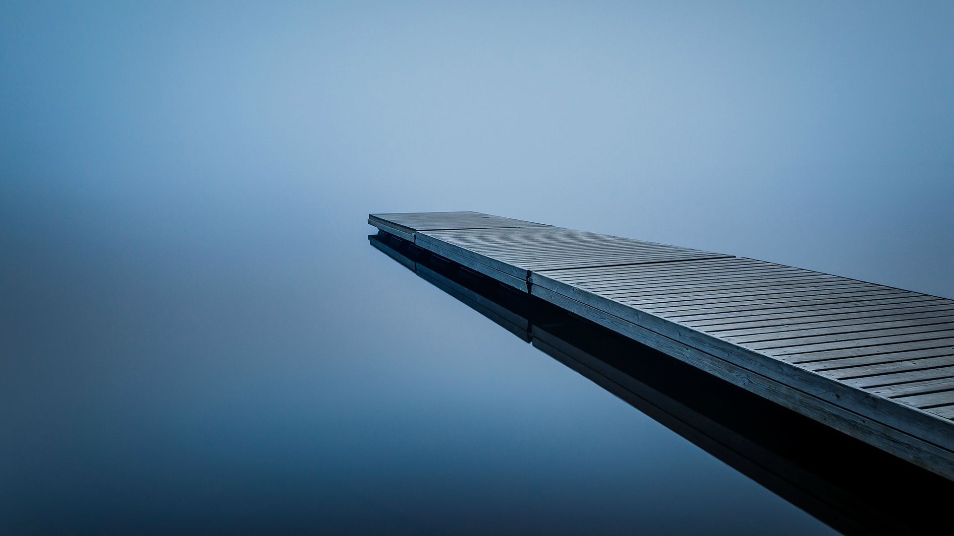 A wooden pier extends into calm blue water HD Wallpaper