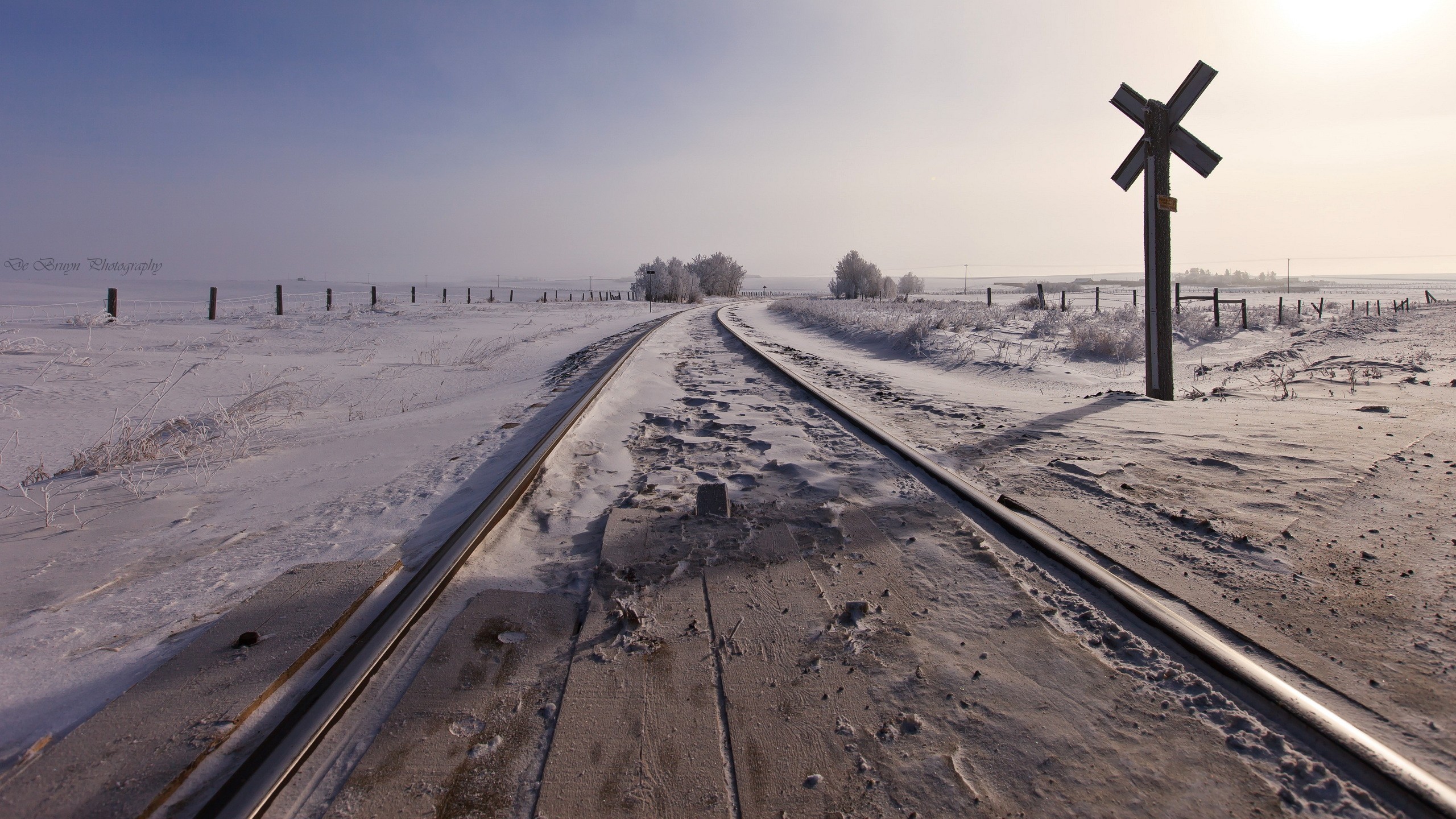Snowy railway tracks with a crossing sign in winter HD Wallpaper