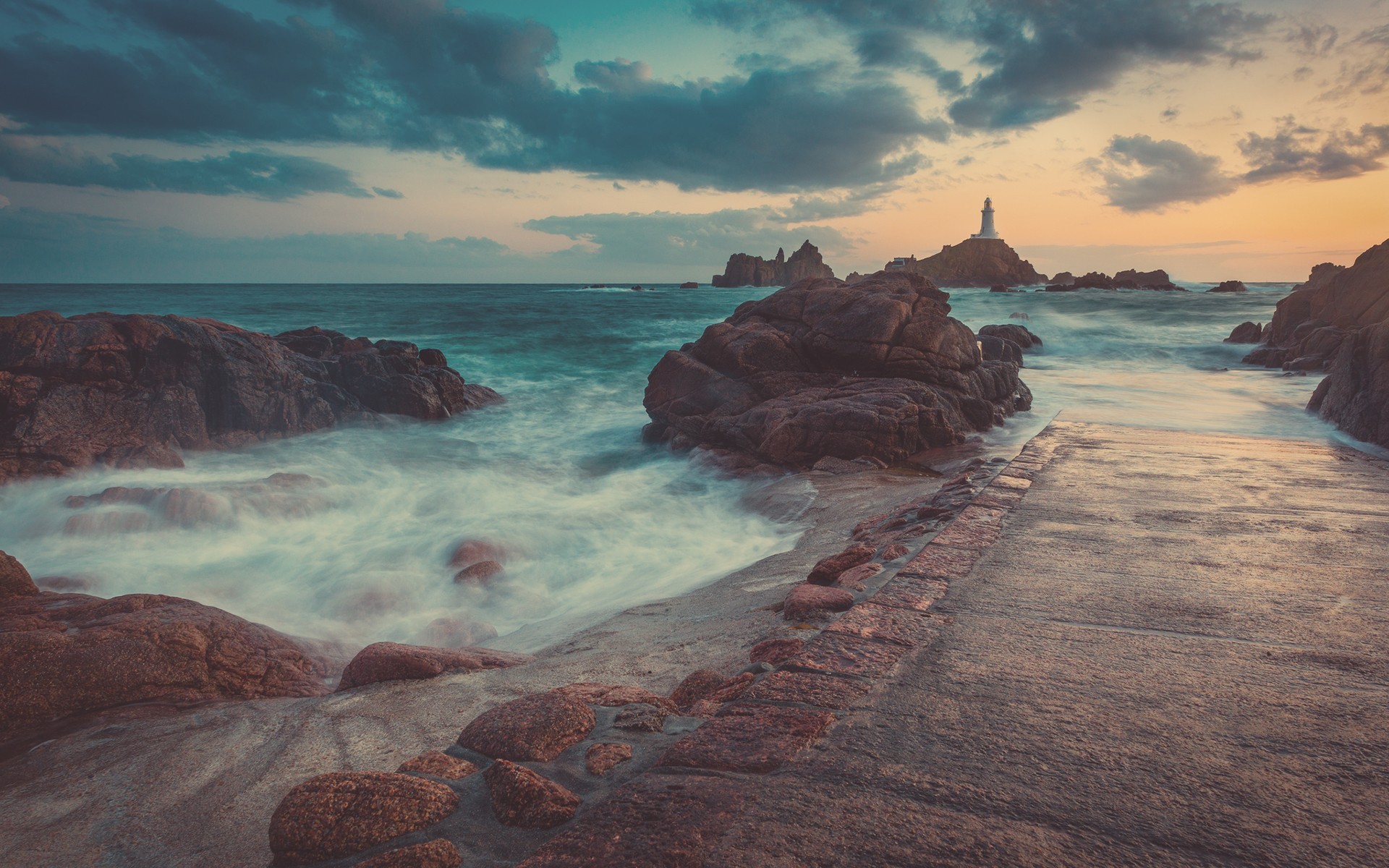 Lighthouse on rocky coast with crashing waves HD Wallpaper