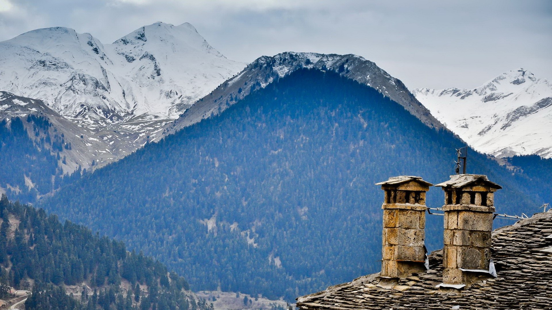 Stone chimneys on a rooftop with snowy mountains in the background HD Wallpaper