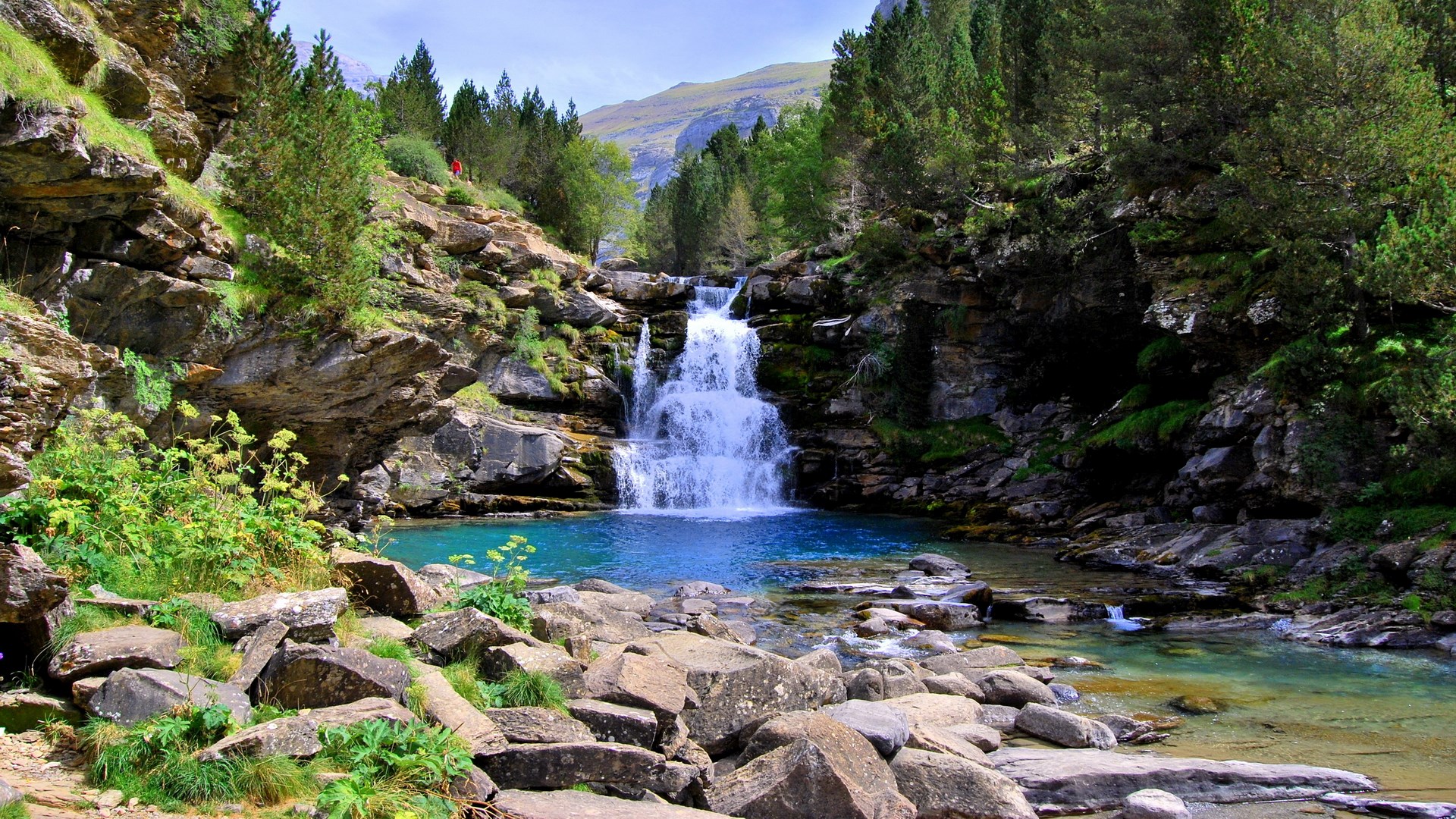 Waterfall cascading into a turquoise pool in a rocky forest HD Wallpaper