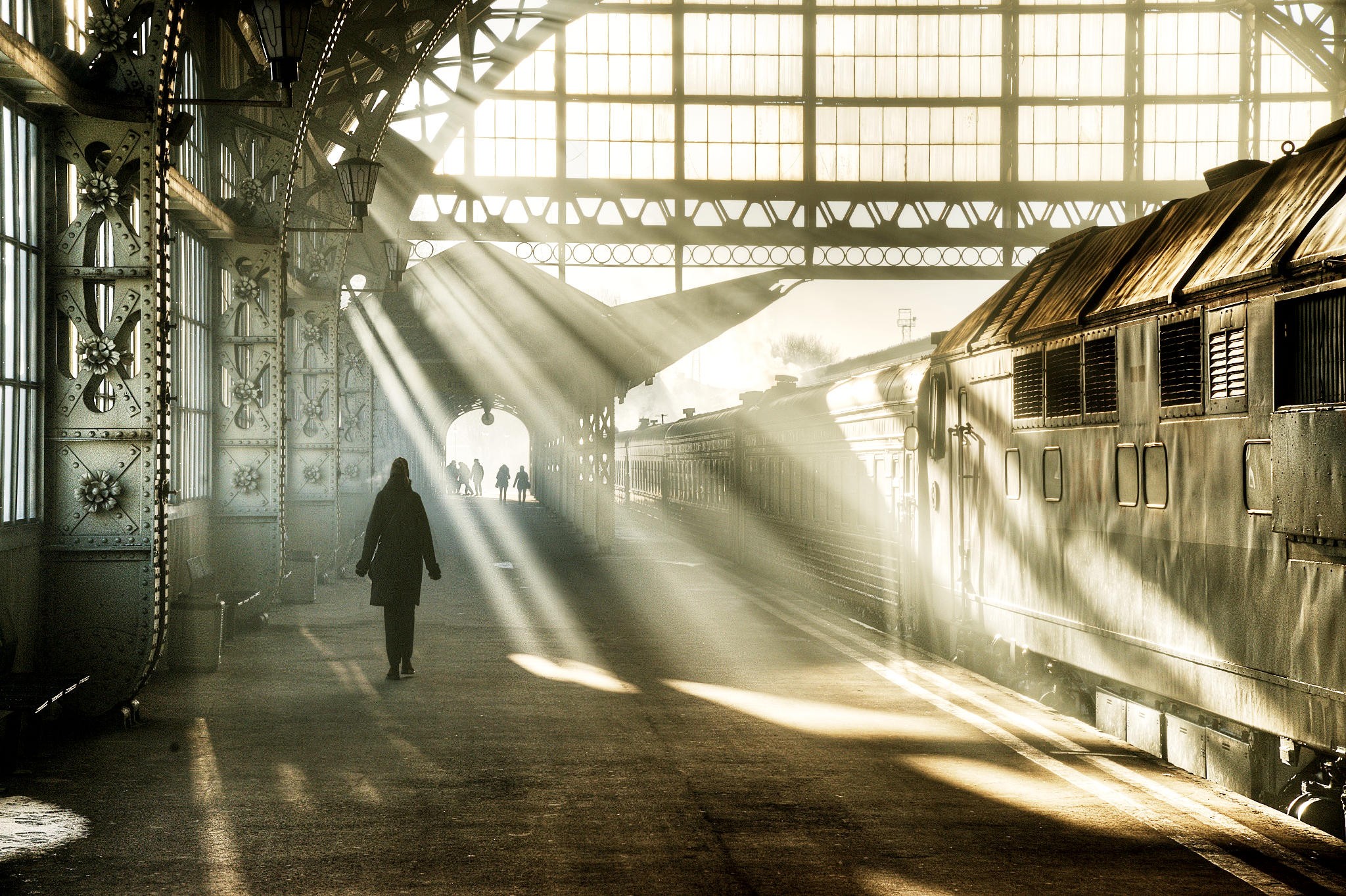 Sunbeams illuminate a train station with a lone figure walking HD Wallpaper