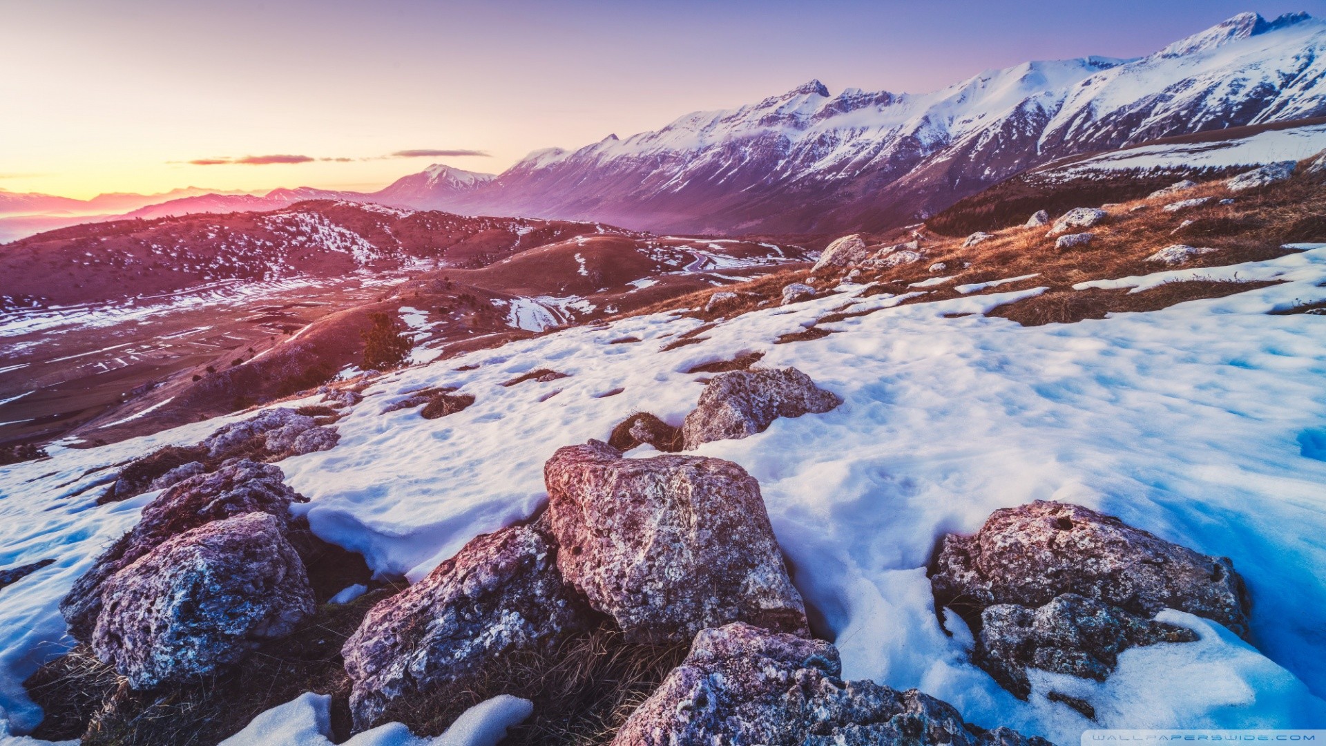 Snowy mountains at sunset with rocks in the foreground HD Wallpaper