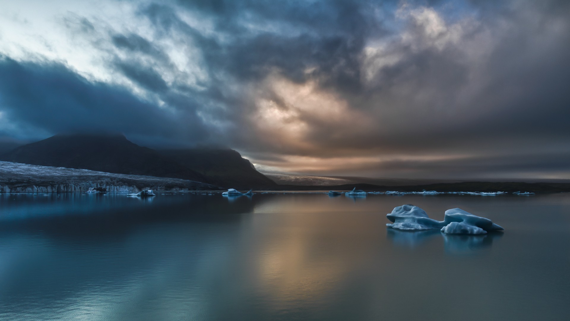 Icebergs floating in a lake with mountains and clouds HD Wallpaper