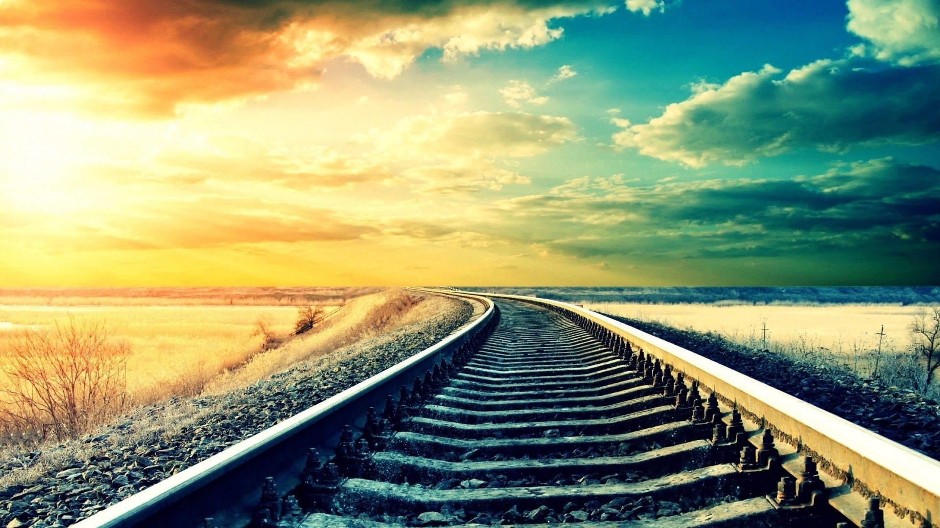 Railroad tracks curve towards a colorful sunset sky HD Wallpaper