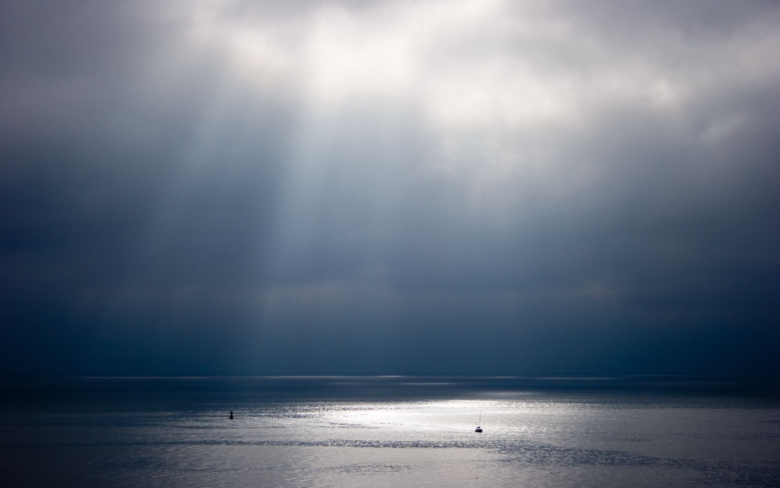 Sun rays breaking through clouds over the sea HD Wallpaper