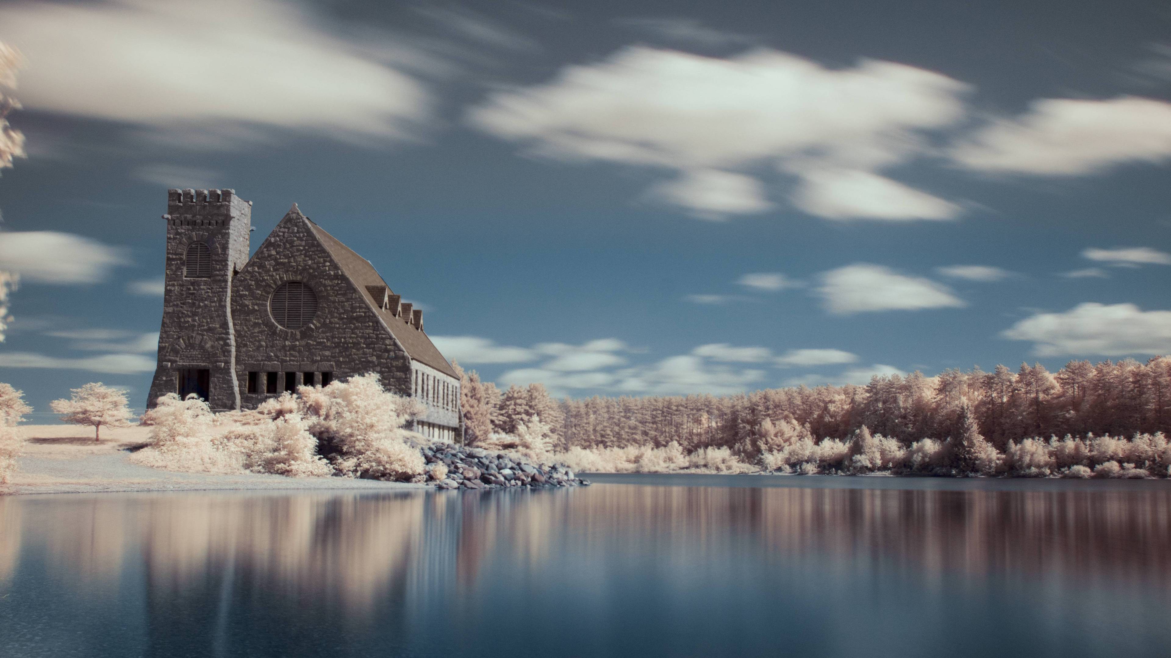 Stone building by a calm lake with white trees and clouds HD Wallpaper