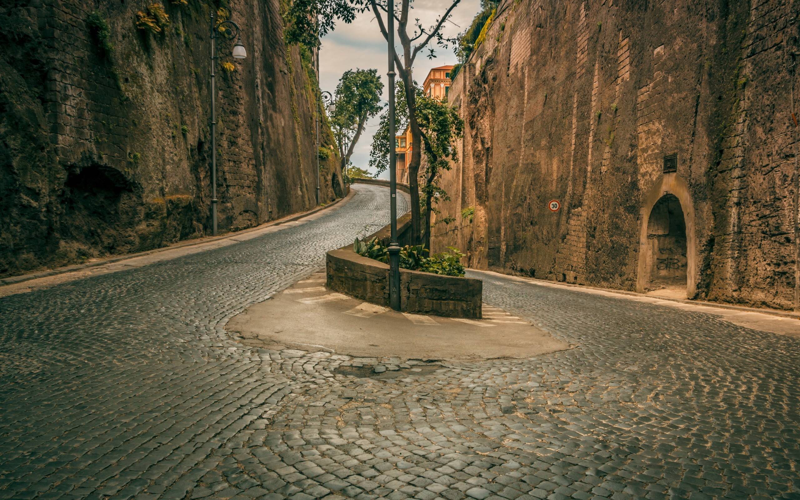 Cobblestone road with hairpin turns between stone walls HD Wallpaper