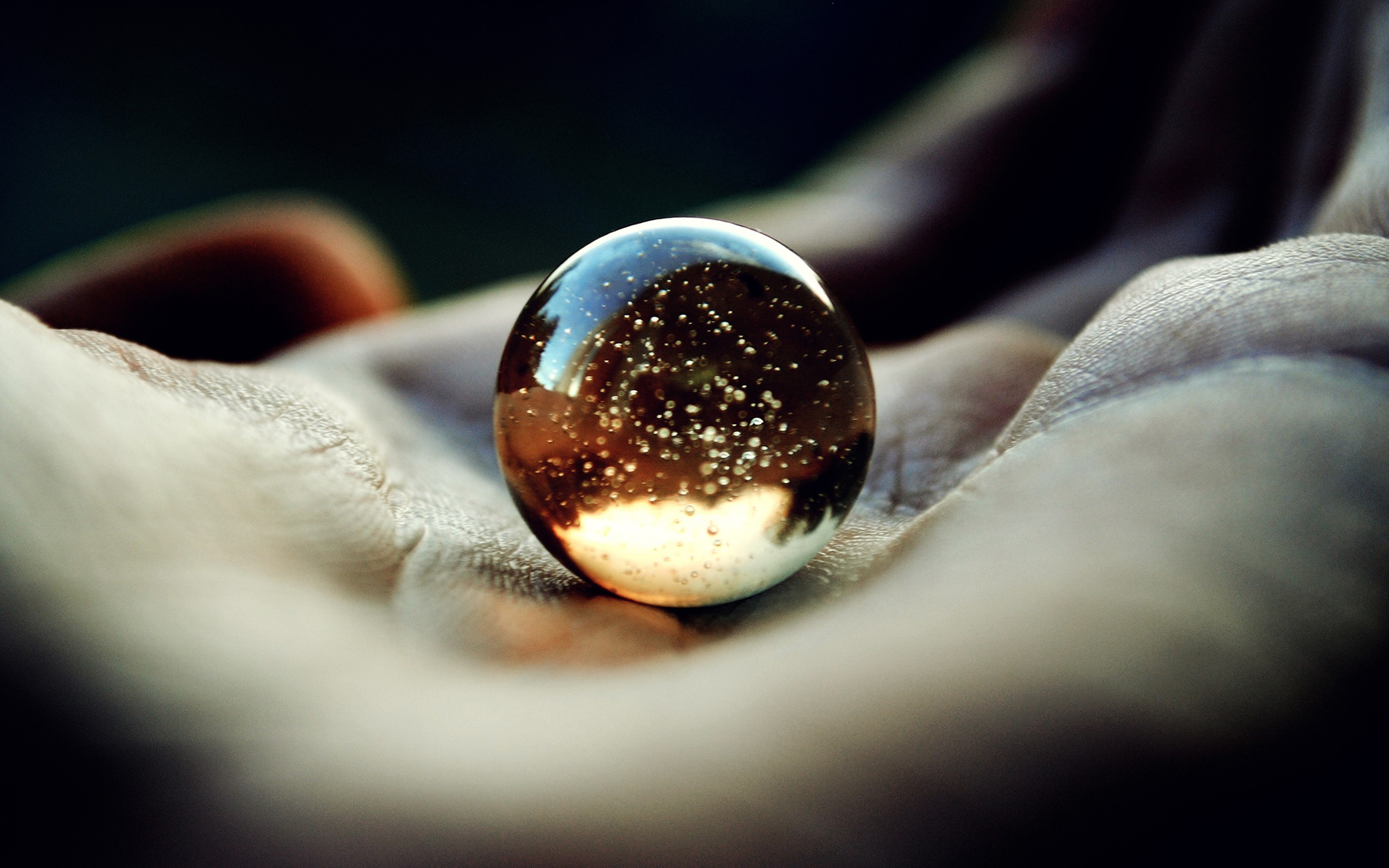 Glass marble with bubbles in a hand HD Wallpaper