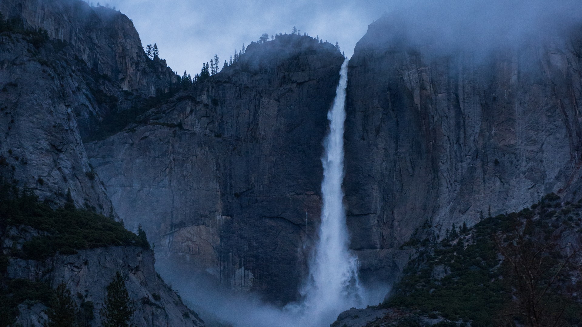 Waterfall cascading down a rocky cliff face with mist HD Wallpaper