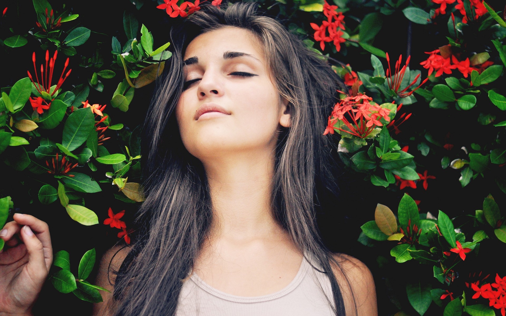 Woman with eyes closed among red flowers and green leaves HD Wallpaper