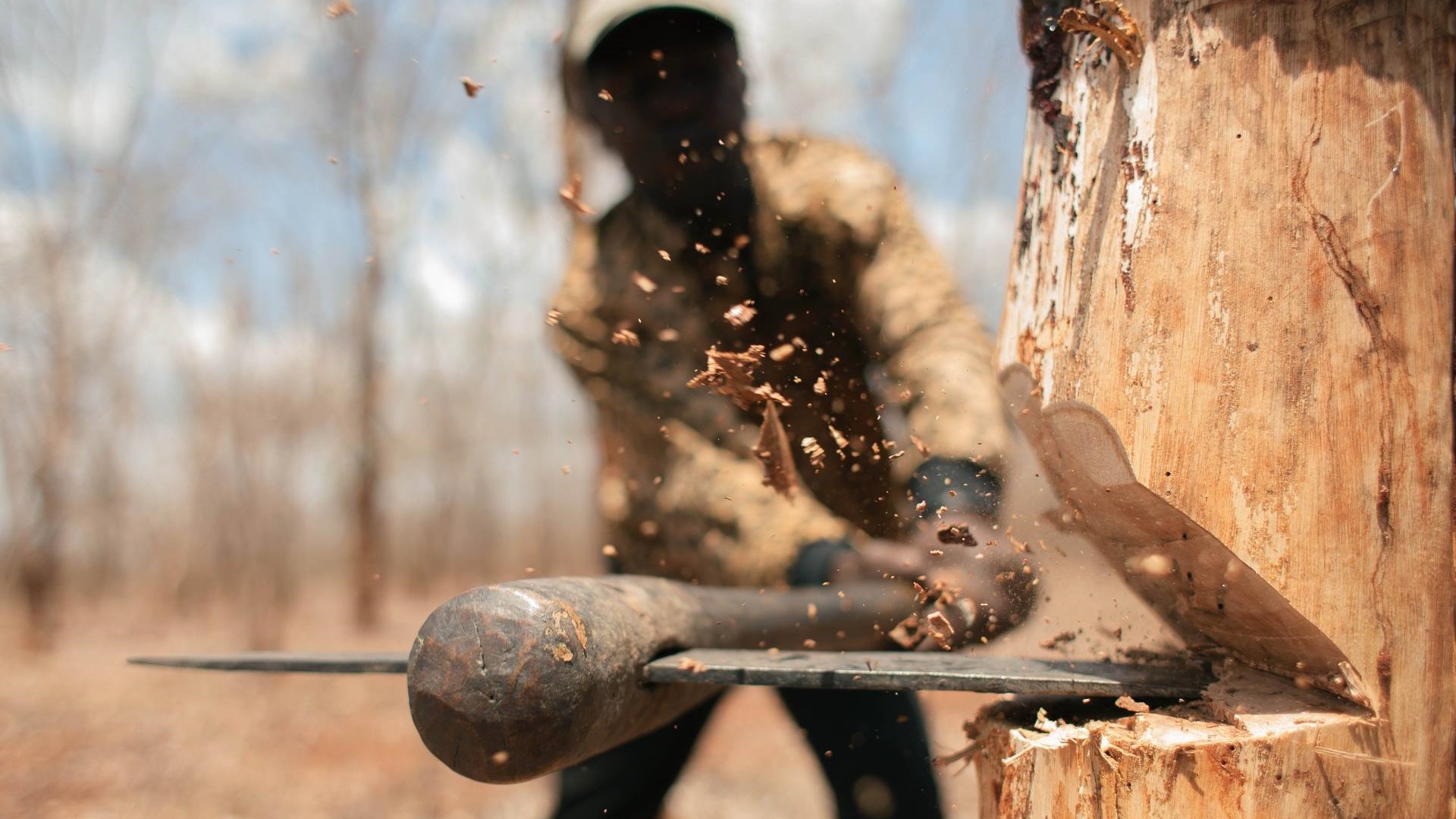 Man chopping wood with an axe, wood splinters flying HD Wallpaper