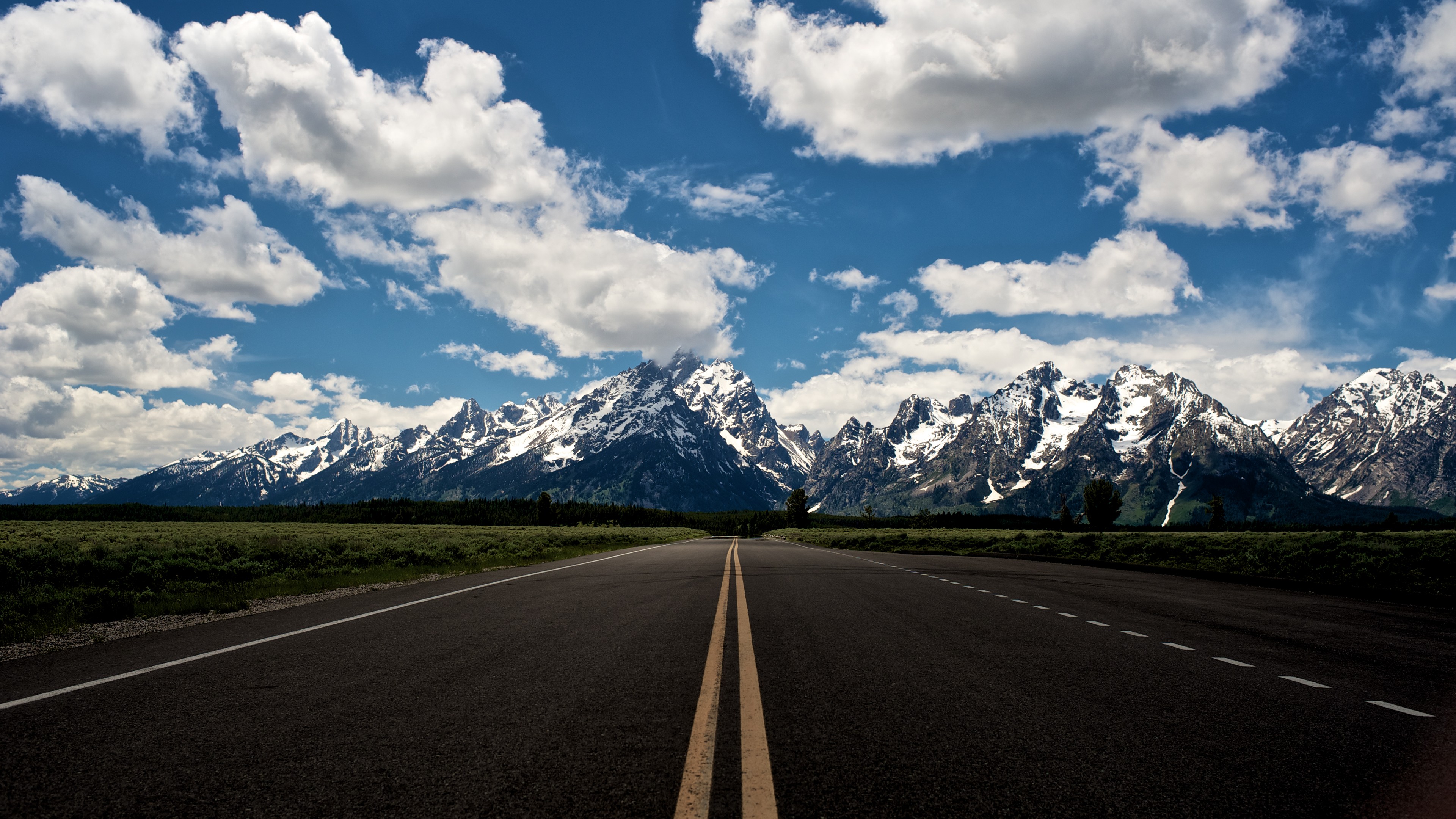 Road leading to snow-capped mountains under a cloudy sky HD Wallpaper