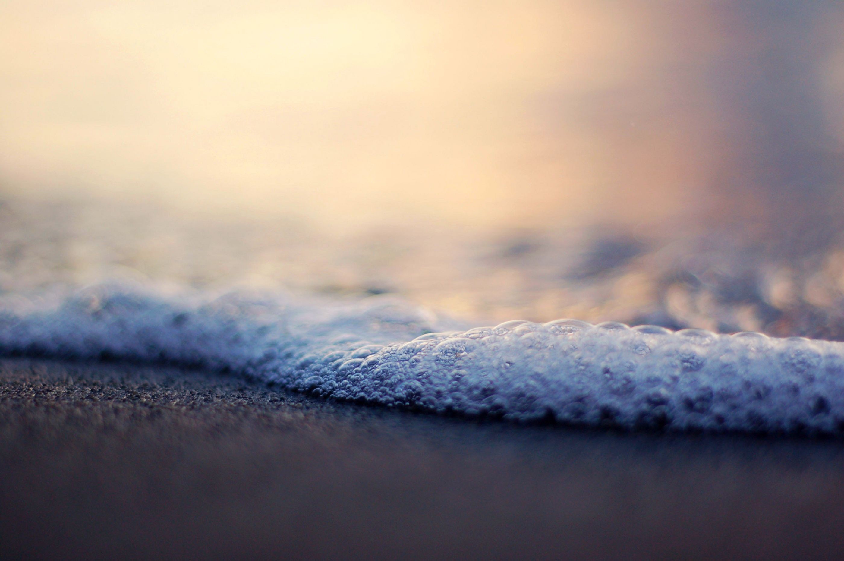 Close-up of ocean waves and bubbles on a beach HD Wallpaper