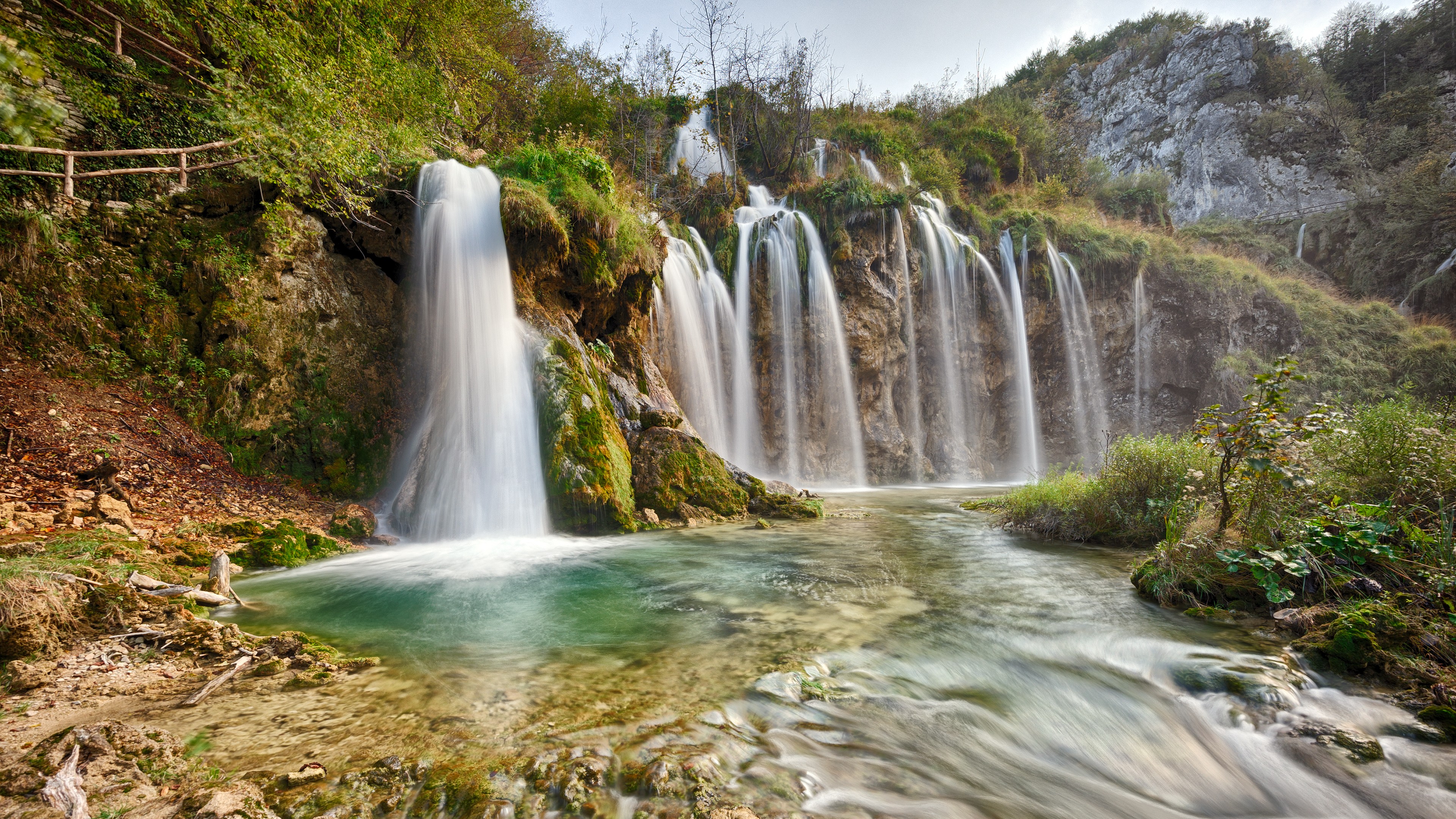 A cascading waterfall flows into a clear pool HD Wallpaper