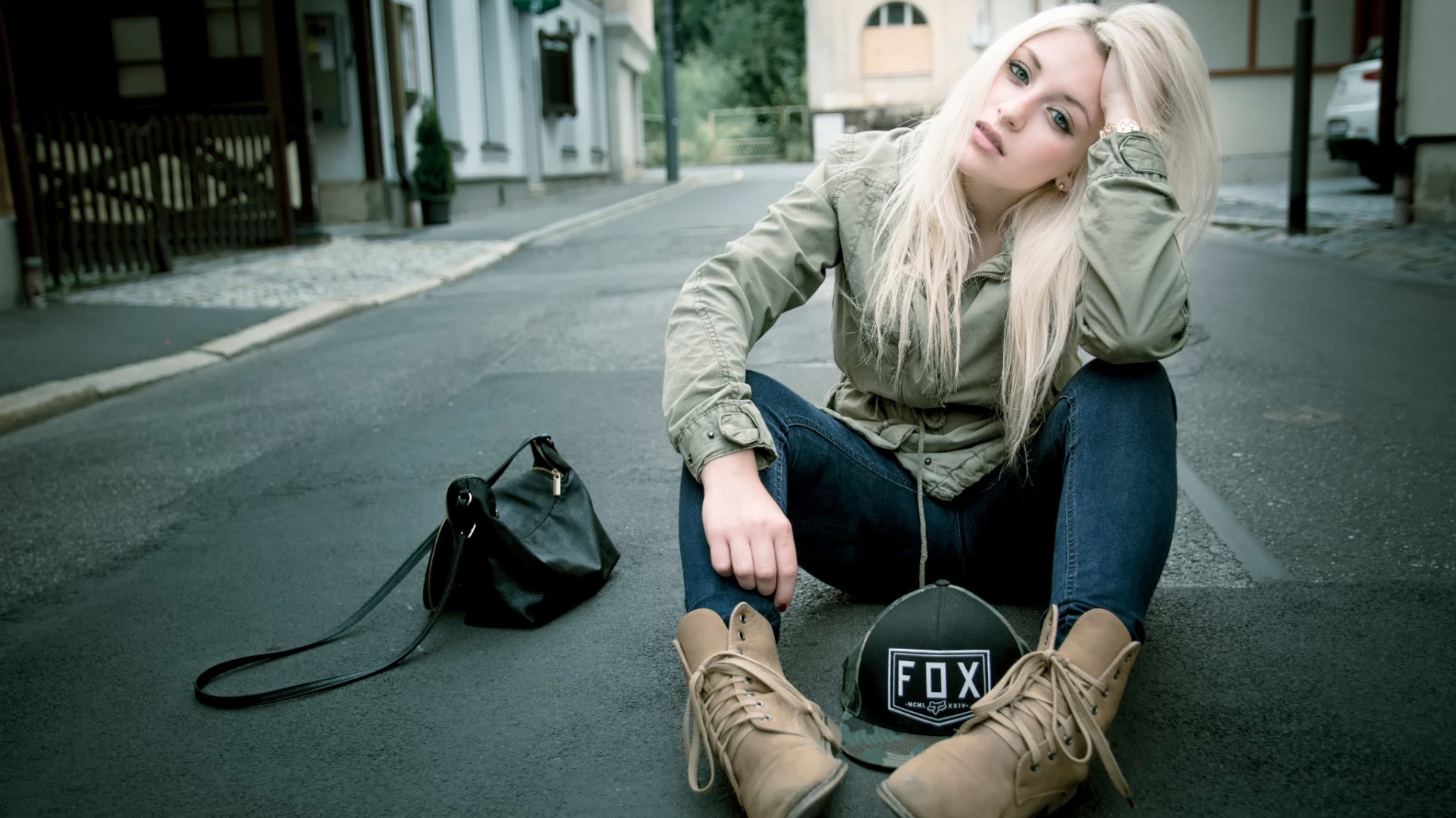 Woman with blonde hair sitting on a city street HD Wallpaper