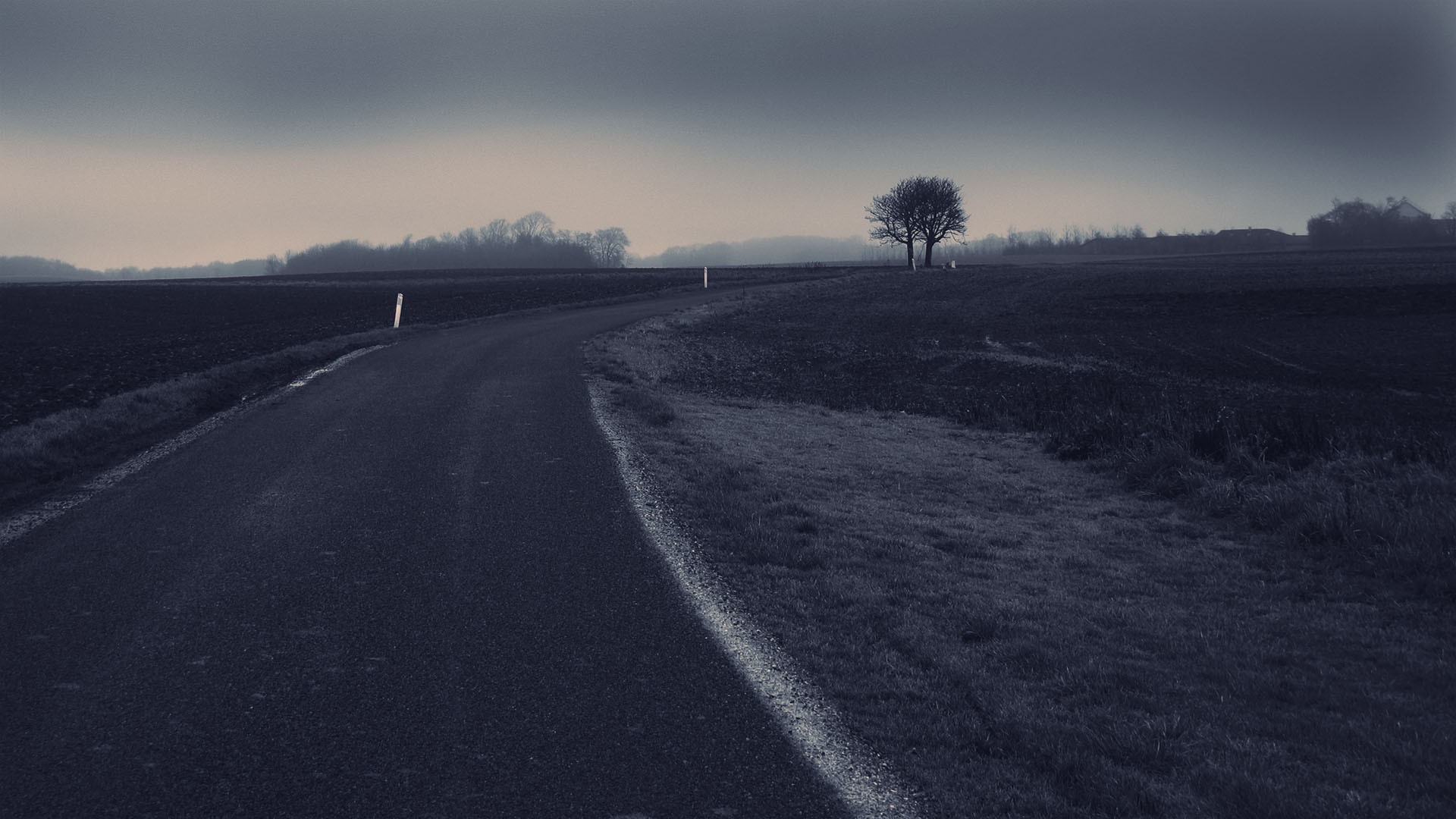 A lonely road through a misty, dark landscape HD Wallpaper