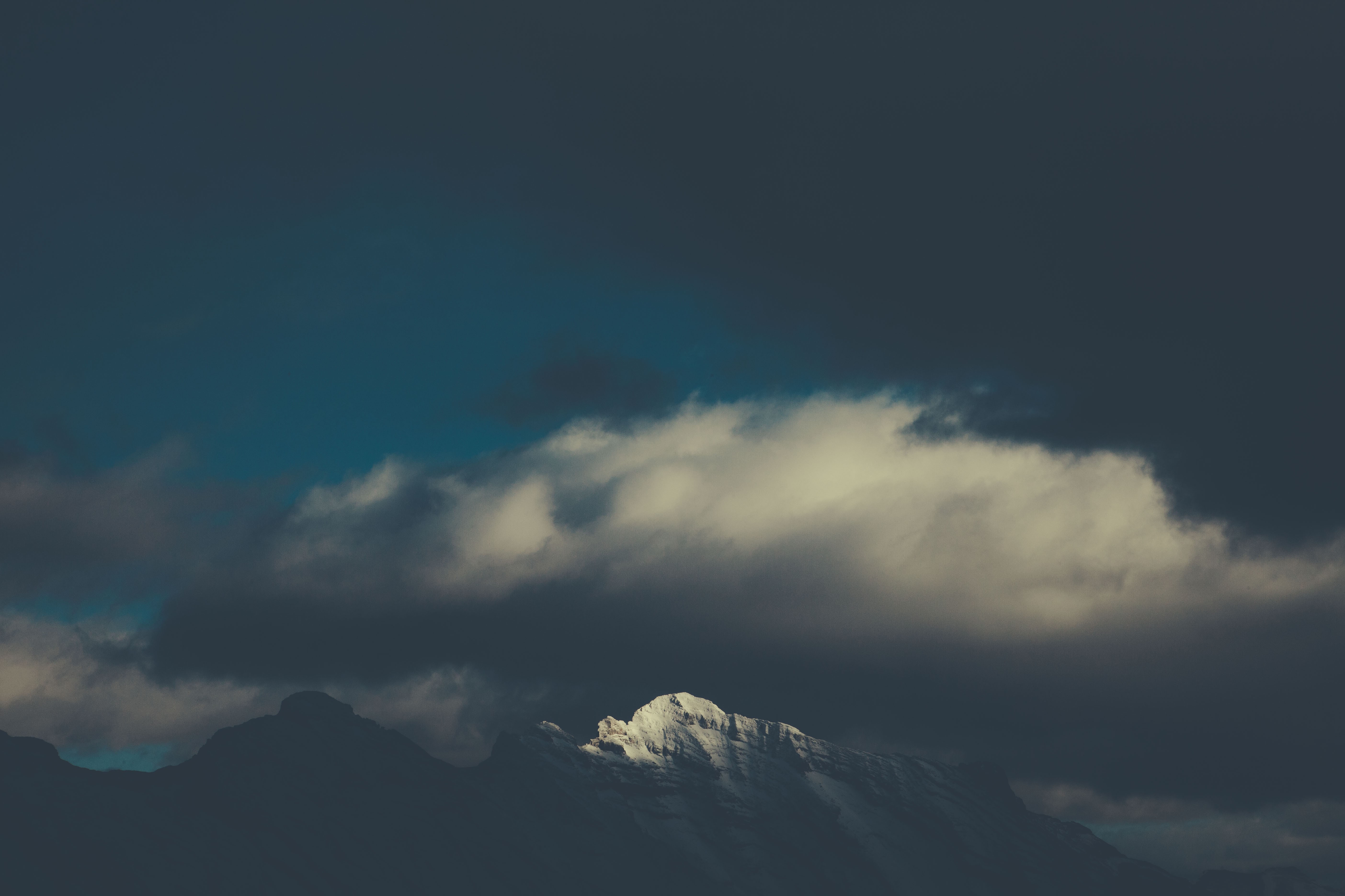 Snow-capped mountains under dark clouds HD Wallpaper