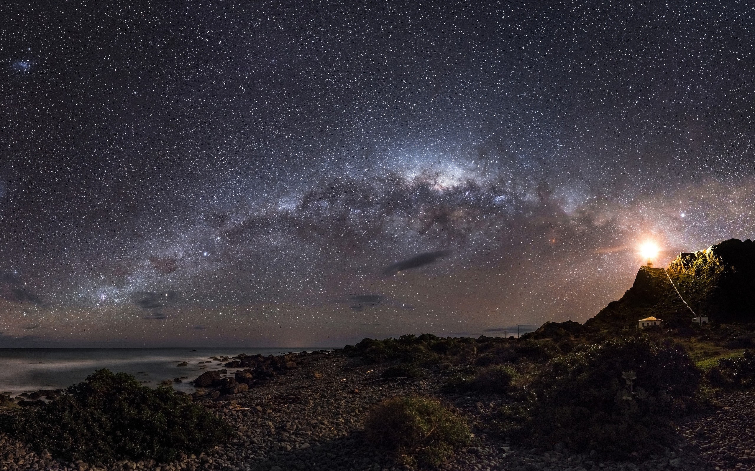 Milky Way over a rocky coastline with a lighthouse HD Wallpaper