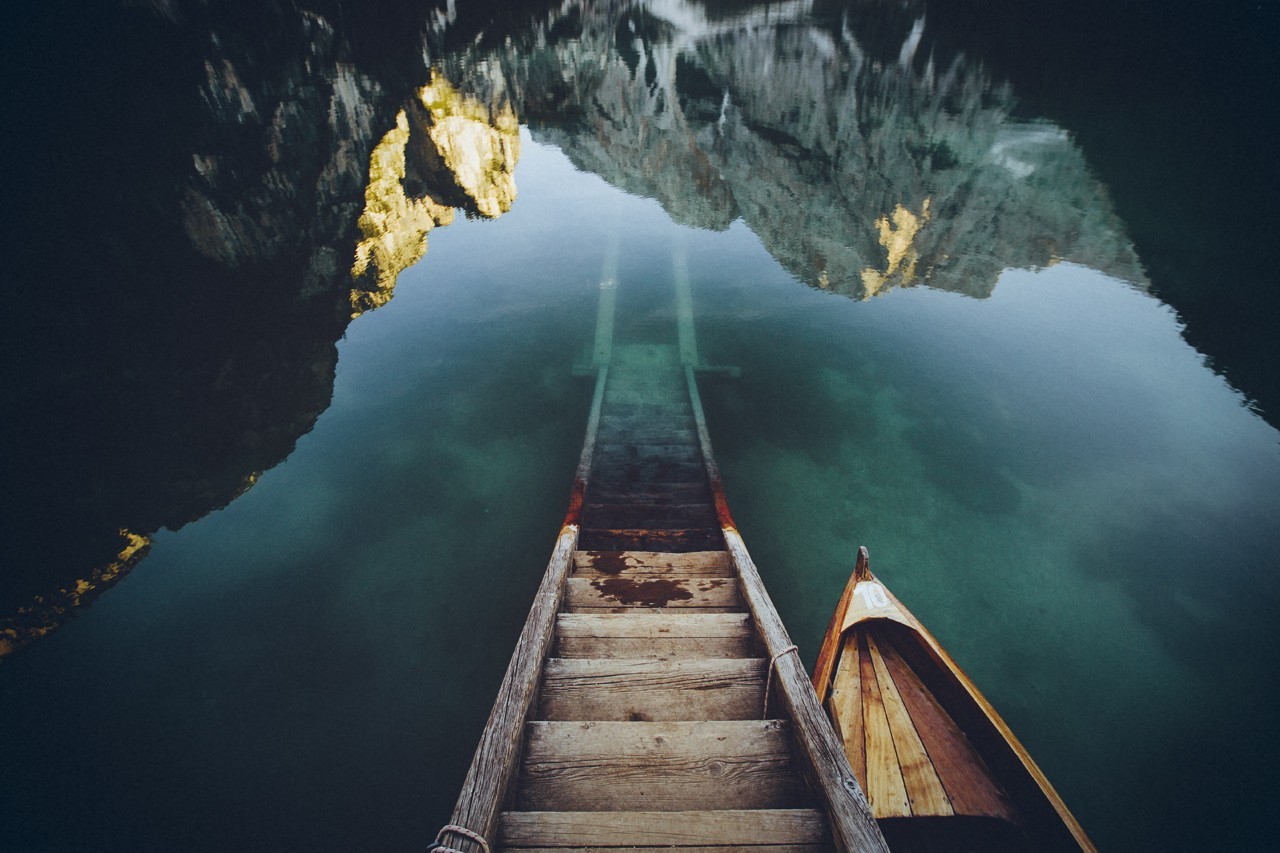 Wooden stairs leading into a clear lake with a boat HD Wallpaper