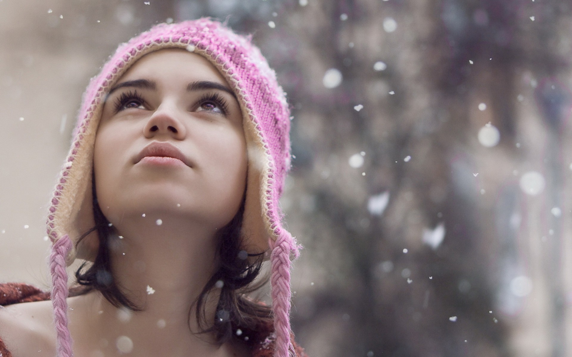 Woman in pink hat looking up at snow HD Wallpaper