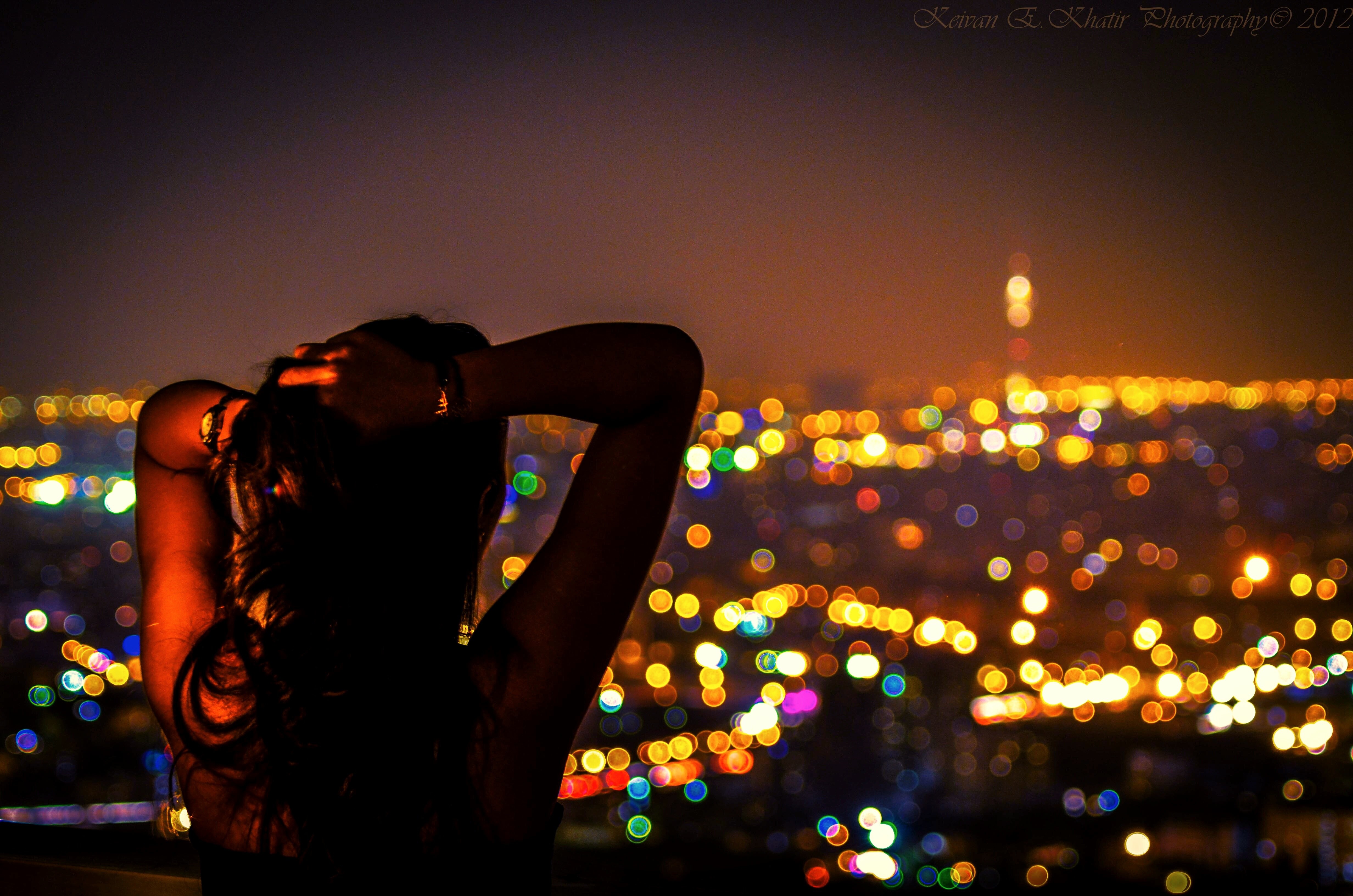 Woman with arms up looking at bokeh city lights at night HD Wallpaper