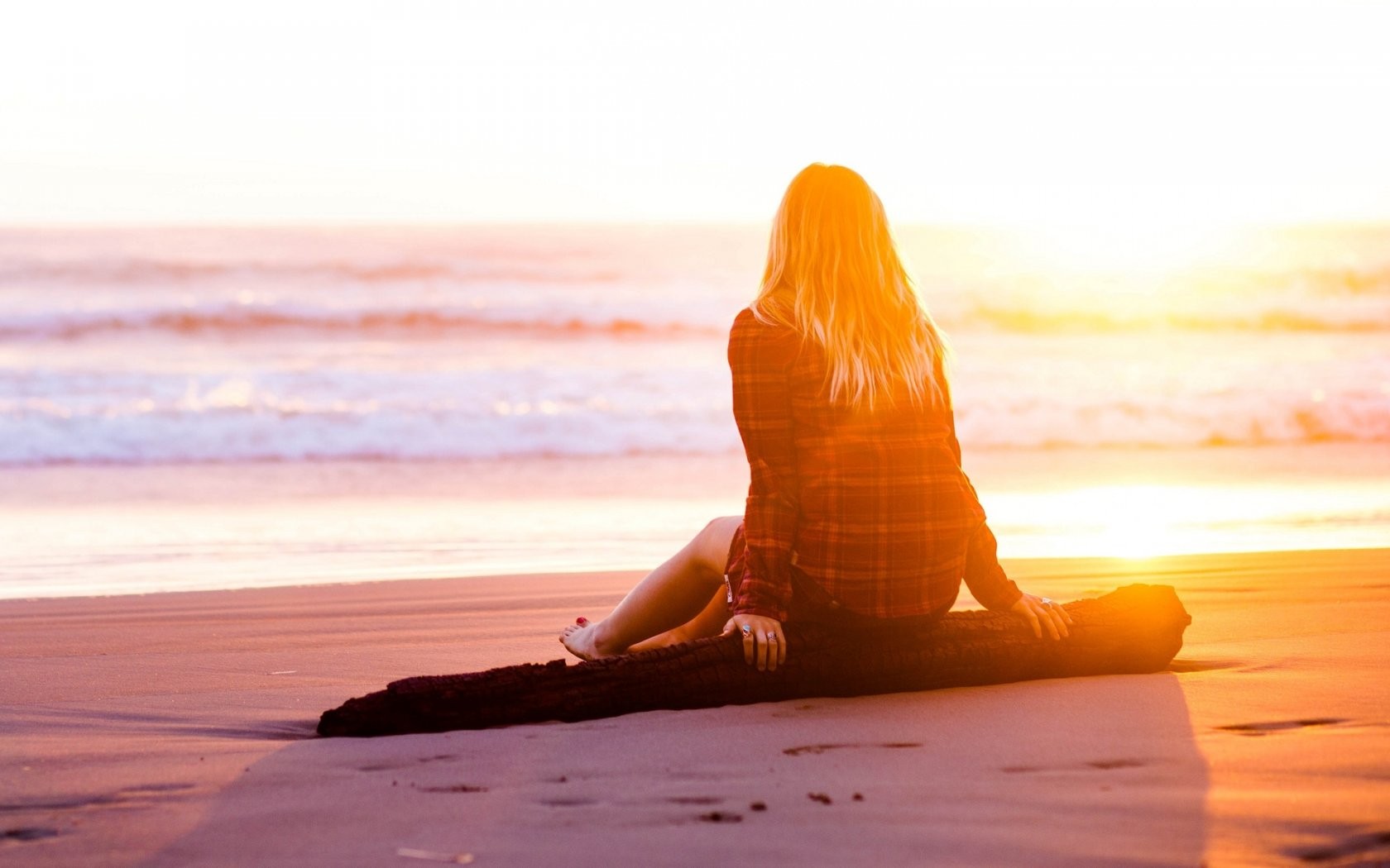Woman sitting on a log at the beach during sunset HD Wallpaper