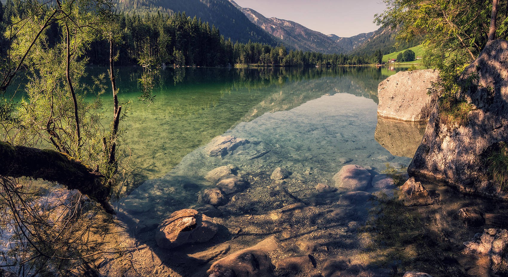 Clear lake with rocky shore and forested mountains HD Wallpaper